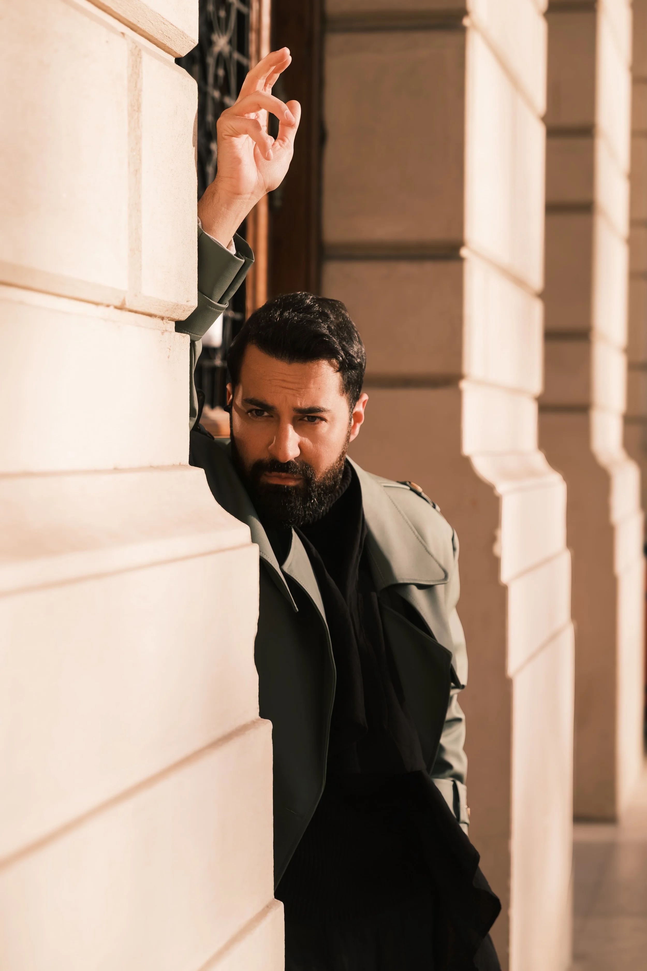A portrait of Ahmed Hatem peeking from behind a beige stone wall, his expression serious, creating a subtle sense of tension.