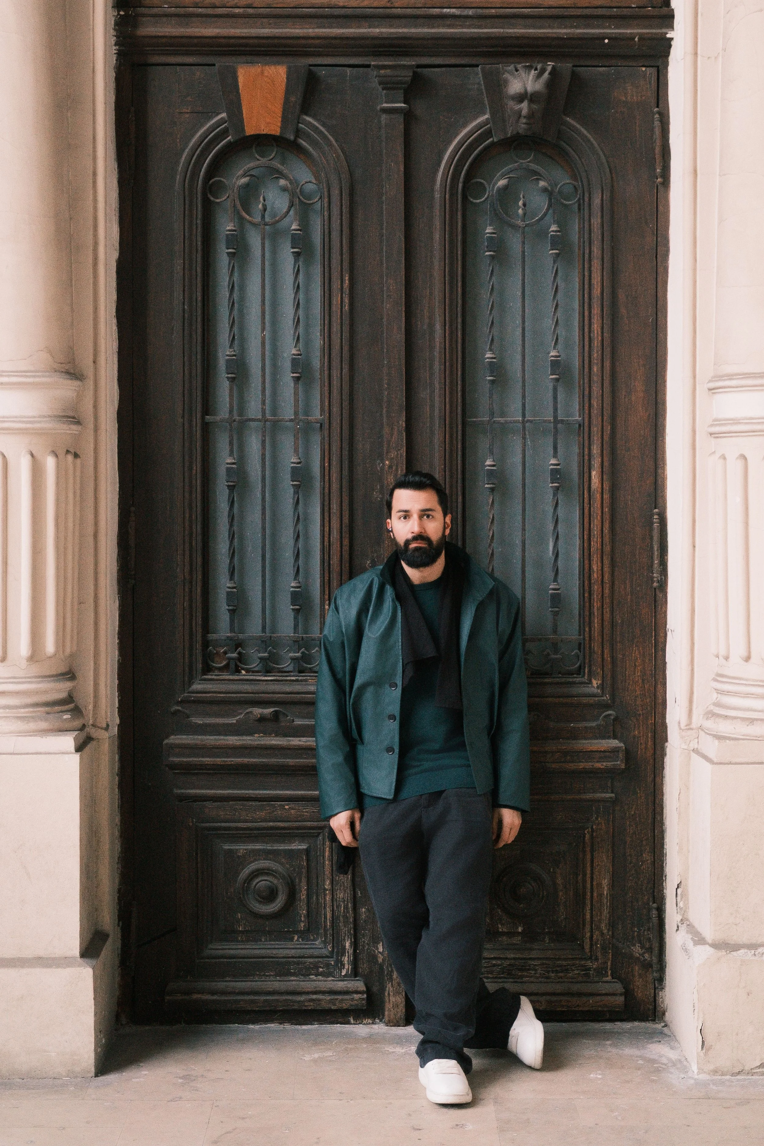 Ahmed Hatem standing in front of a dark wooden door inside a classical building, surrounded by symmetry and soft tones.