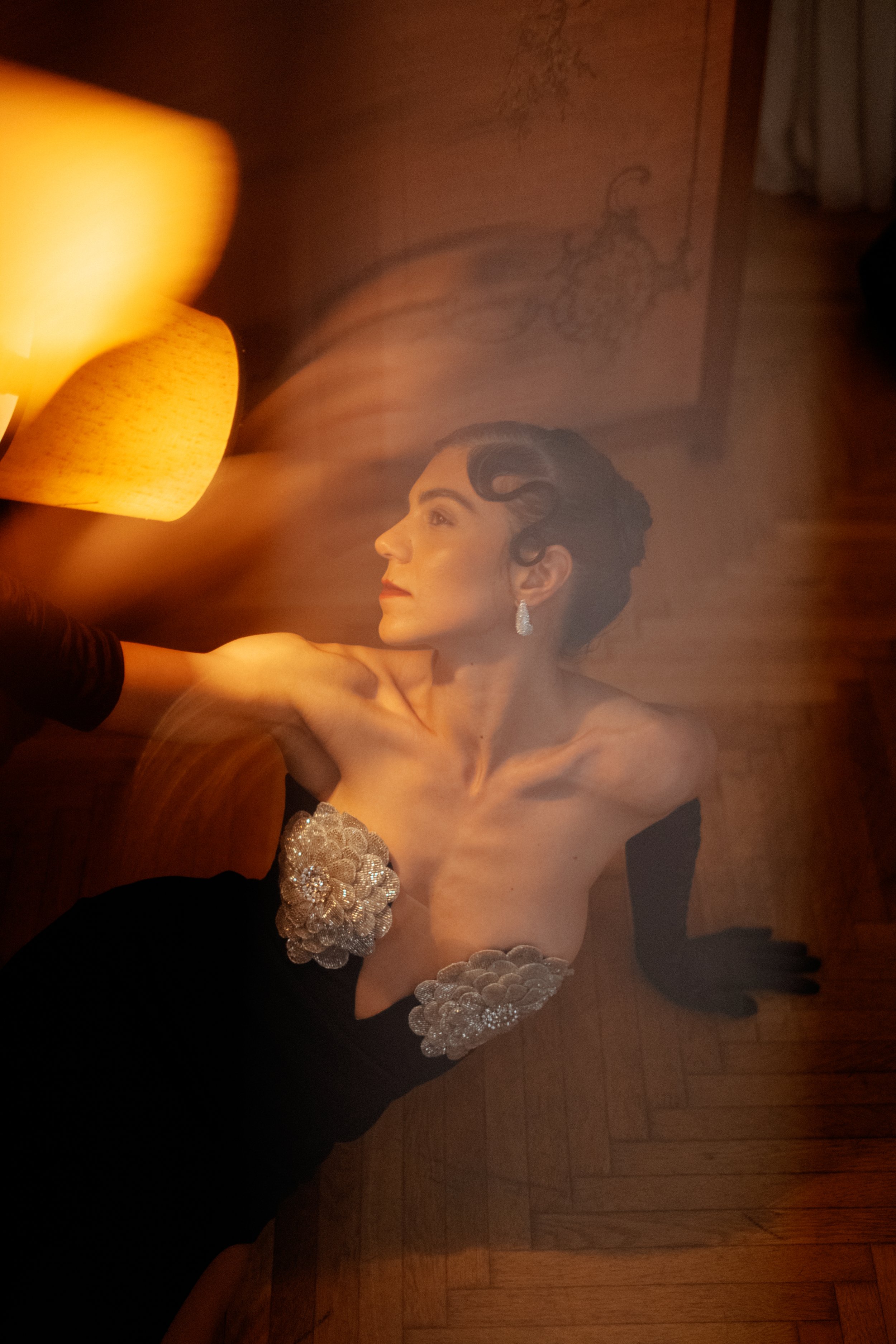 Warm toned glass distortion portrait of Sorina Rotaru in a dark dress with sequined floral detail, lamp light