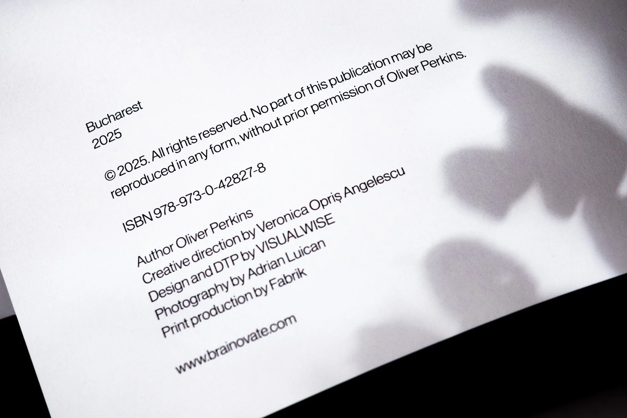 Close-up of a printed copyright page with publication details, author information, and website, cast in shadow on the right side.