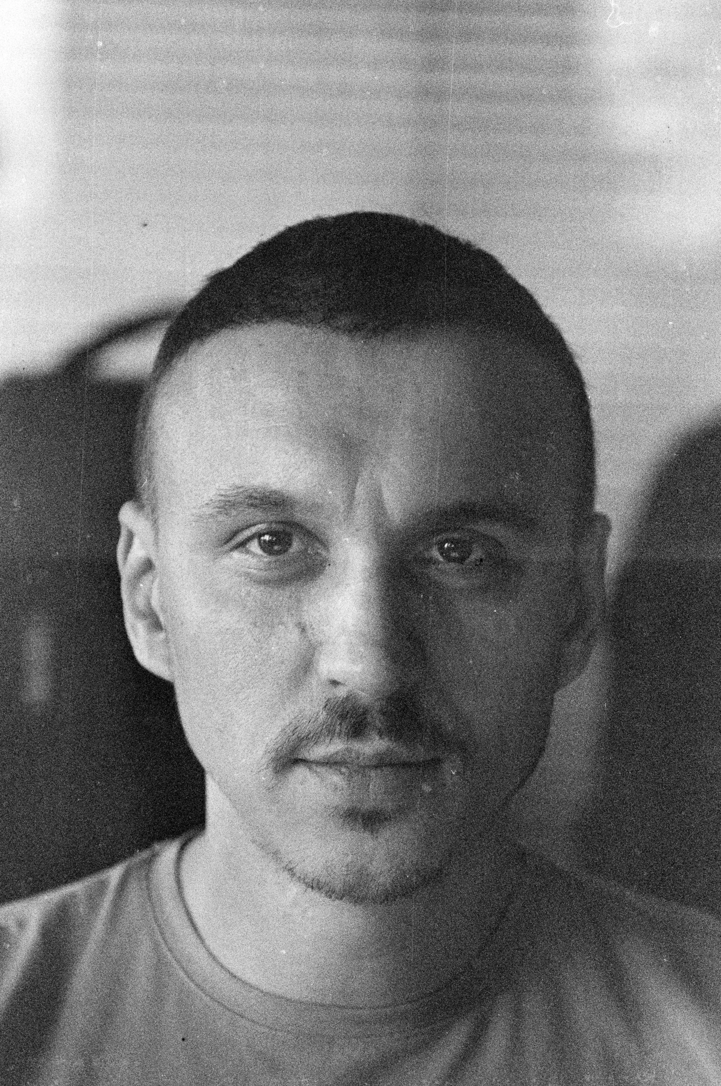 Black and white portrait of a young man with short hair, a mustache, and a goatee, looking directly at the camera.