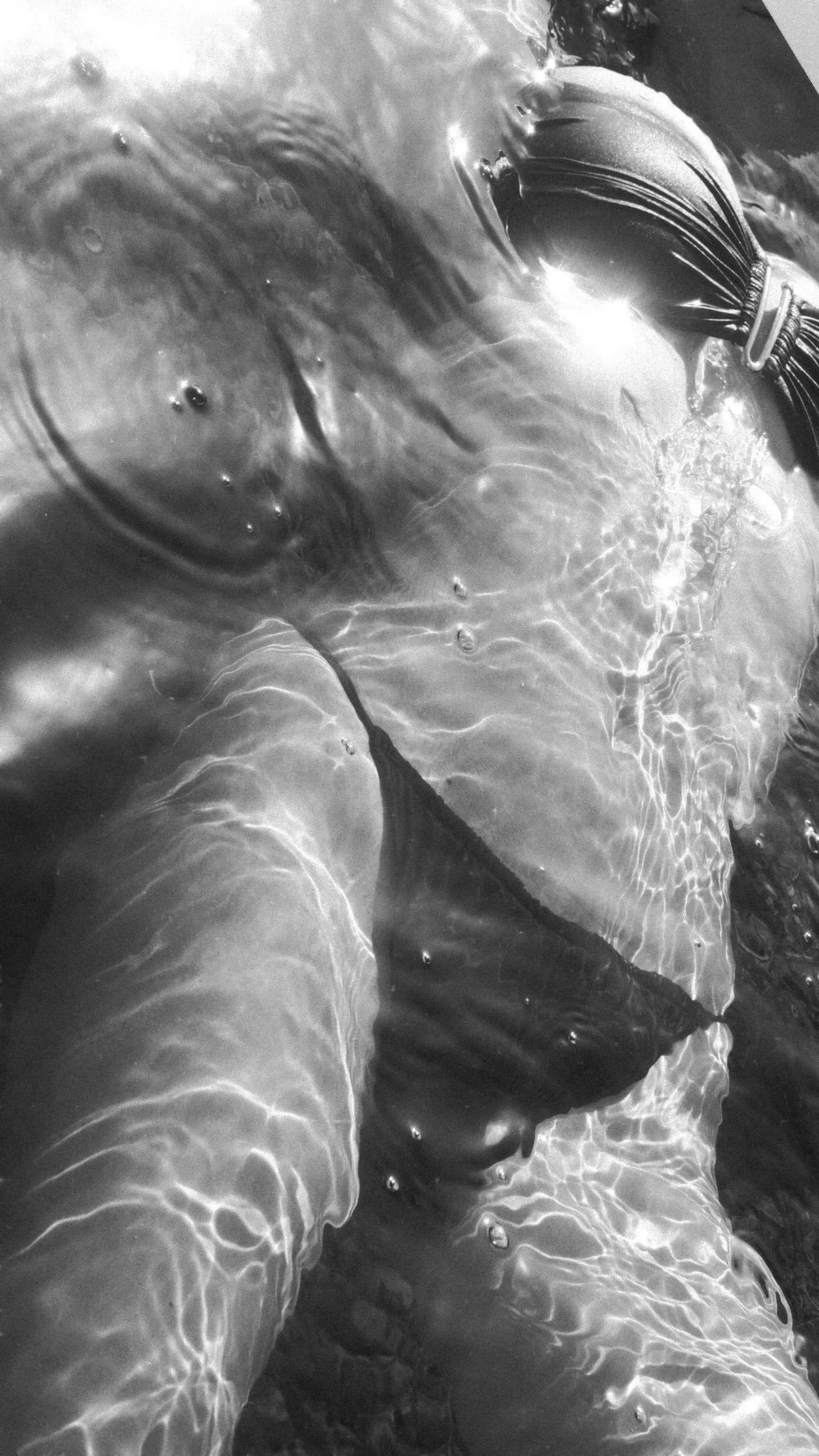 A person wearing a swimsuit is floating in water, visible from the shoulders down, with sunlight creating ripples and reflections on the water surface.