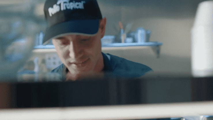 A man in a blue cap with text 'Mr. Trucker' on it, working in a food truck or kitchen.