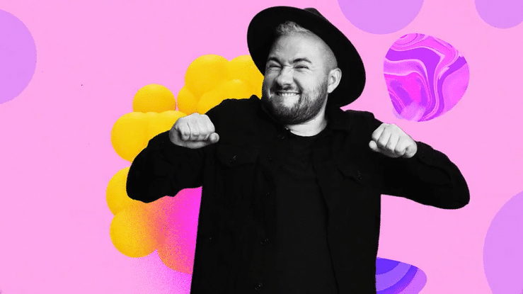 Man smiling and flexing his arms, wearing a black hat and black jacket, with a colorful abstract background.