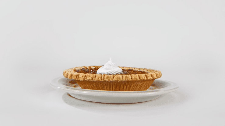 A slice of pumpkin pie with whipped cream on top on a white plate against a white background.