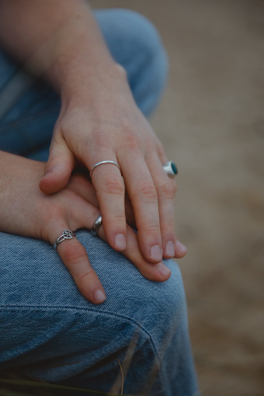Close-up of two peReiki healing reiki drumming lowestoft suffolk norfolk east angliaople's hands with rings resting on a person's lap in blue jeans.