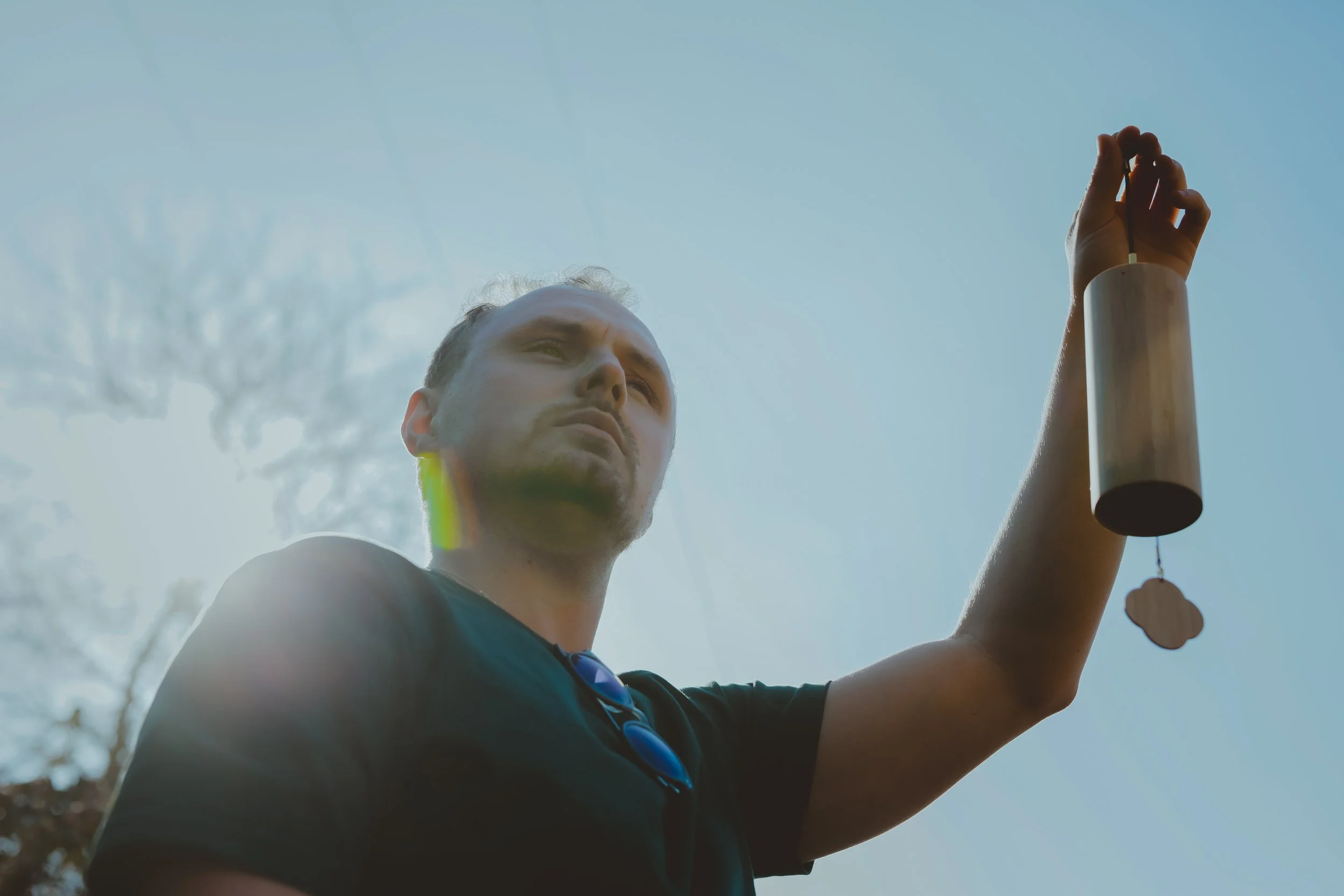 A man holding a wind chime outdoors against a clear blue sky.