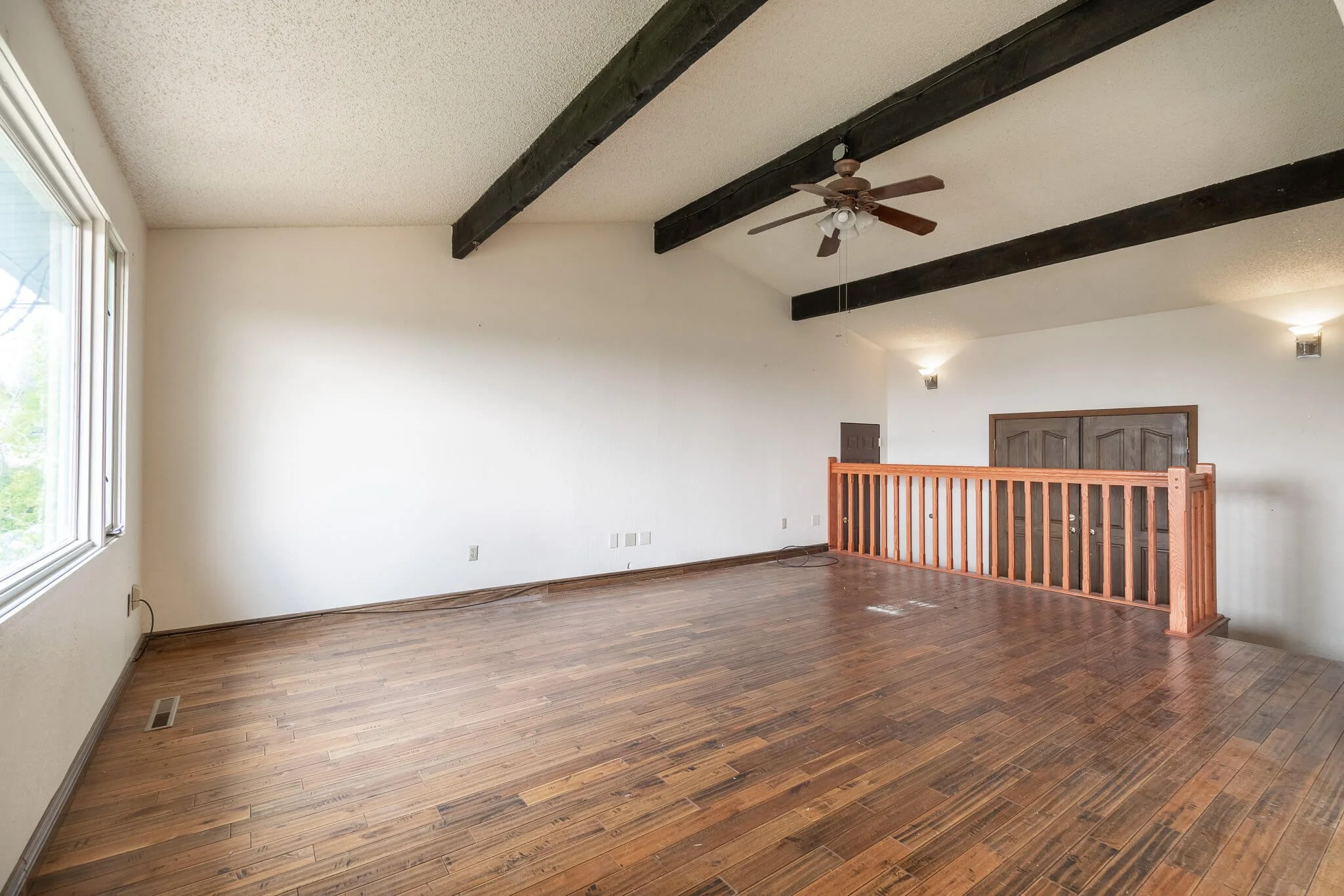 Original living room before renovation showing lowered entry, interior railing, exposed beams, and wood flooring in a Great Falls Montana home