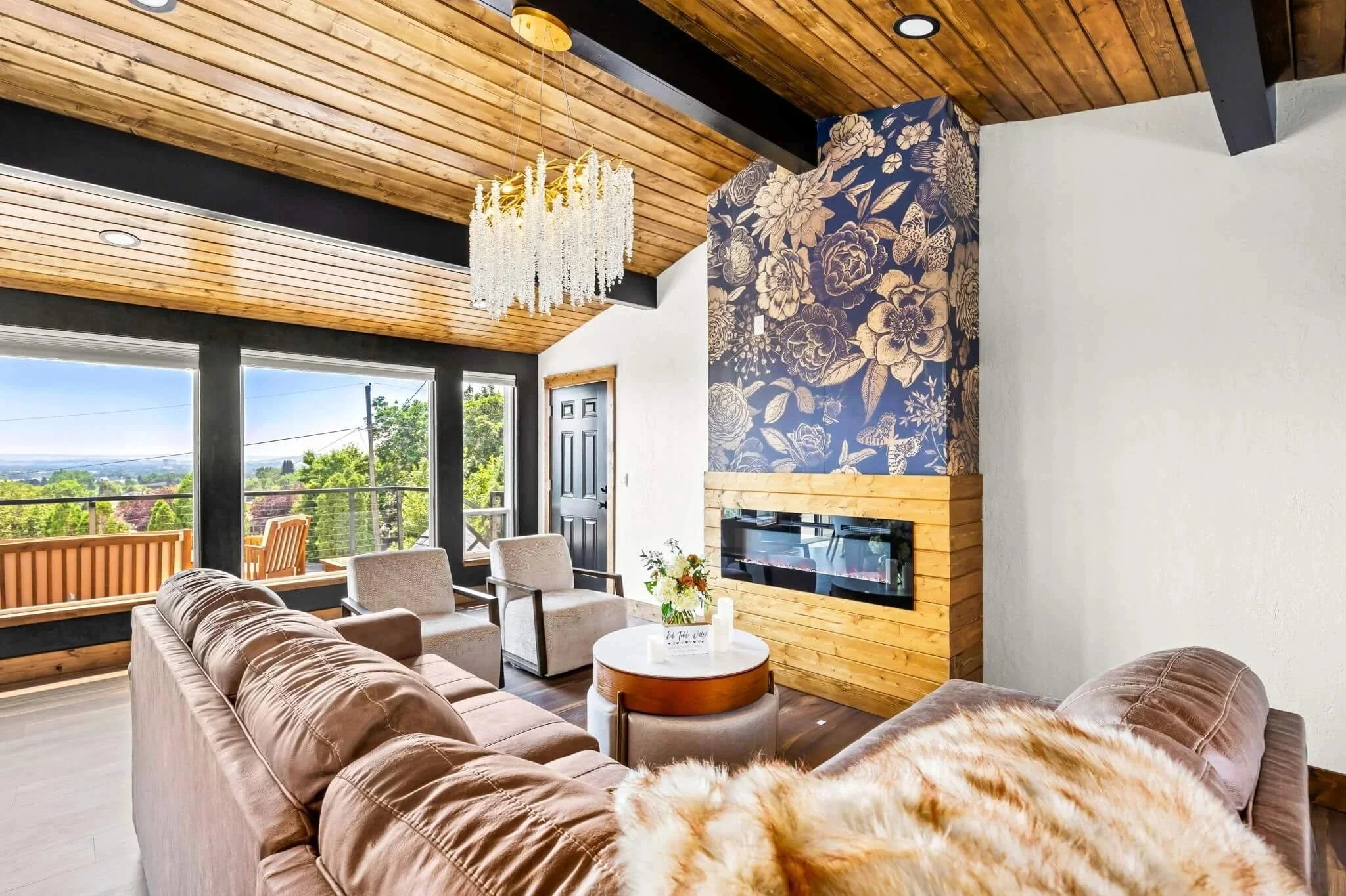 Light-filled living room with wood ceiling, black beams, statement fireplace, and large windows in a renovated Great Falls, Montana home.