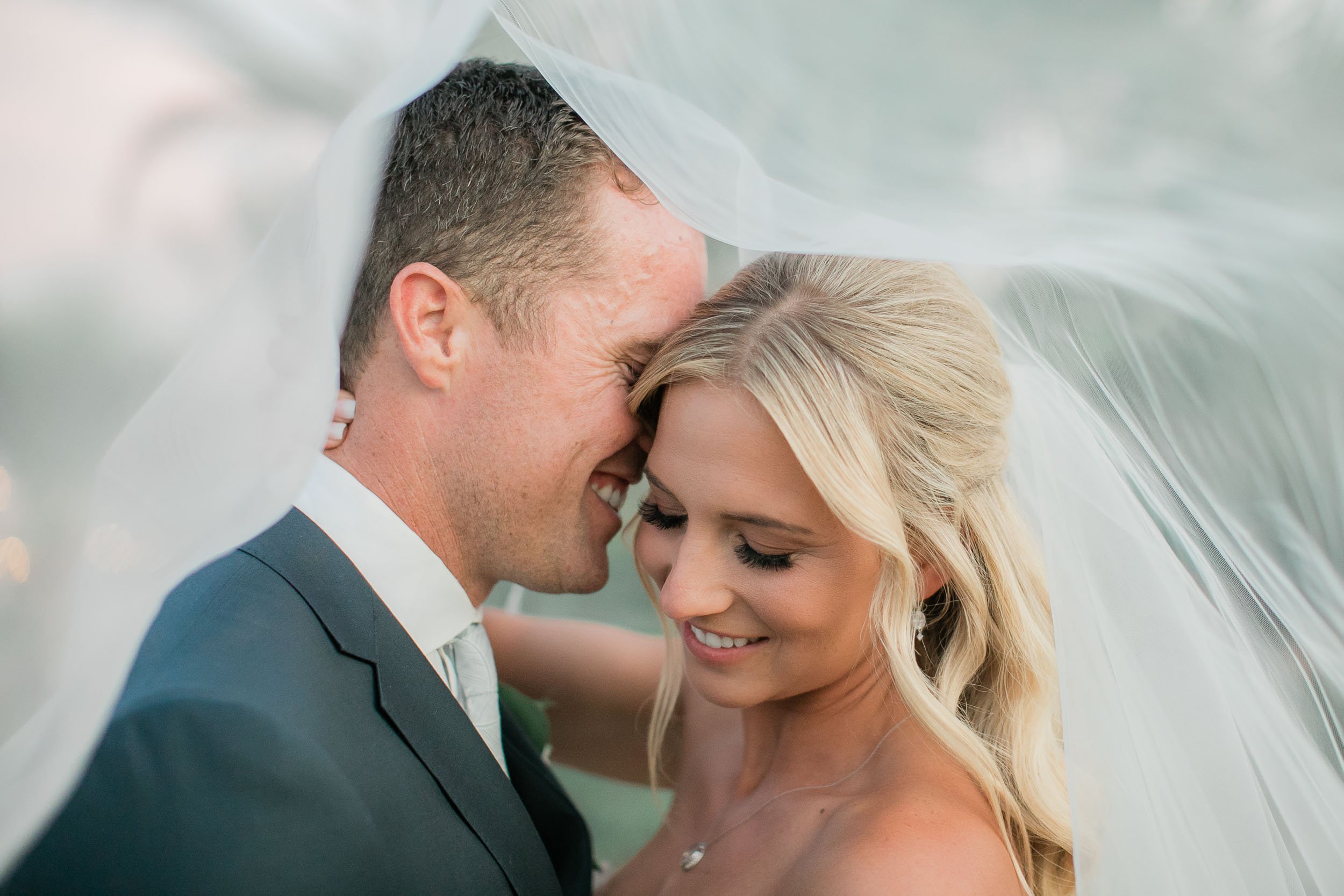 Bride and groom embracing under veil, smiling, close-up.