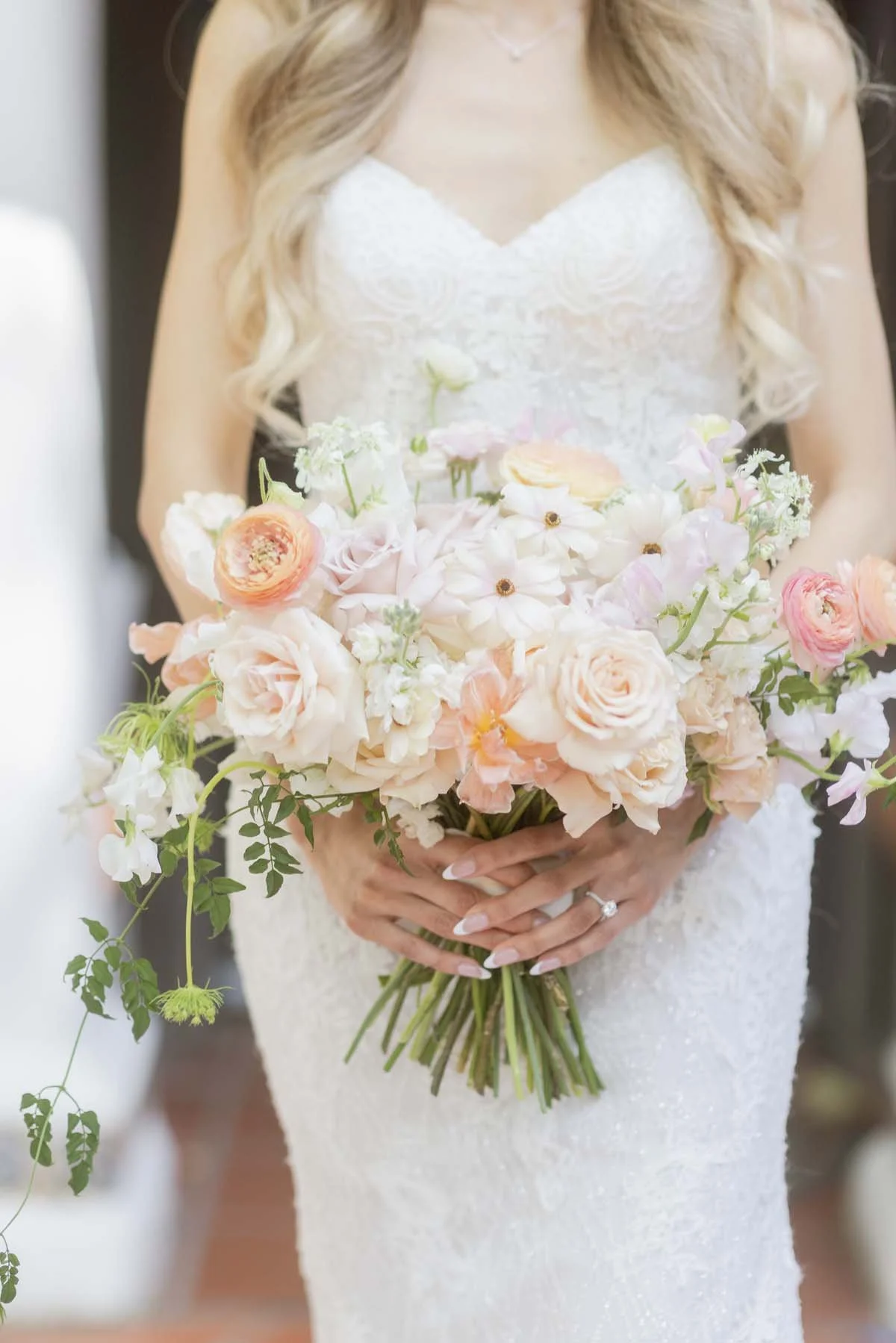 Bride holding bouquet of white and peach flowers, wearing lace wedding dress.