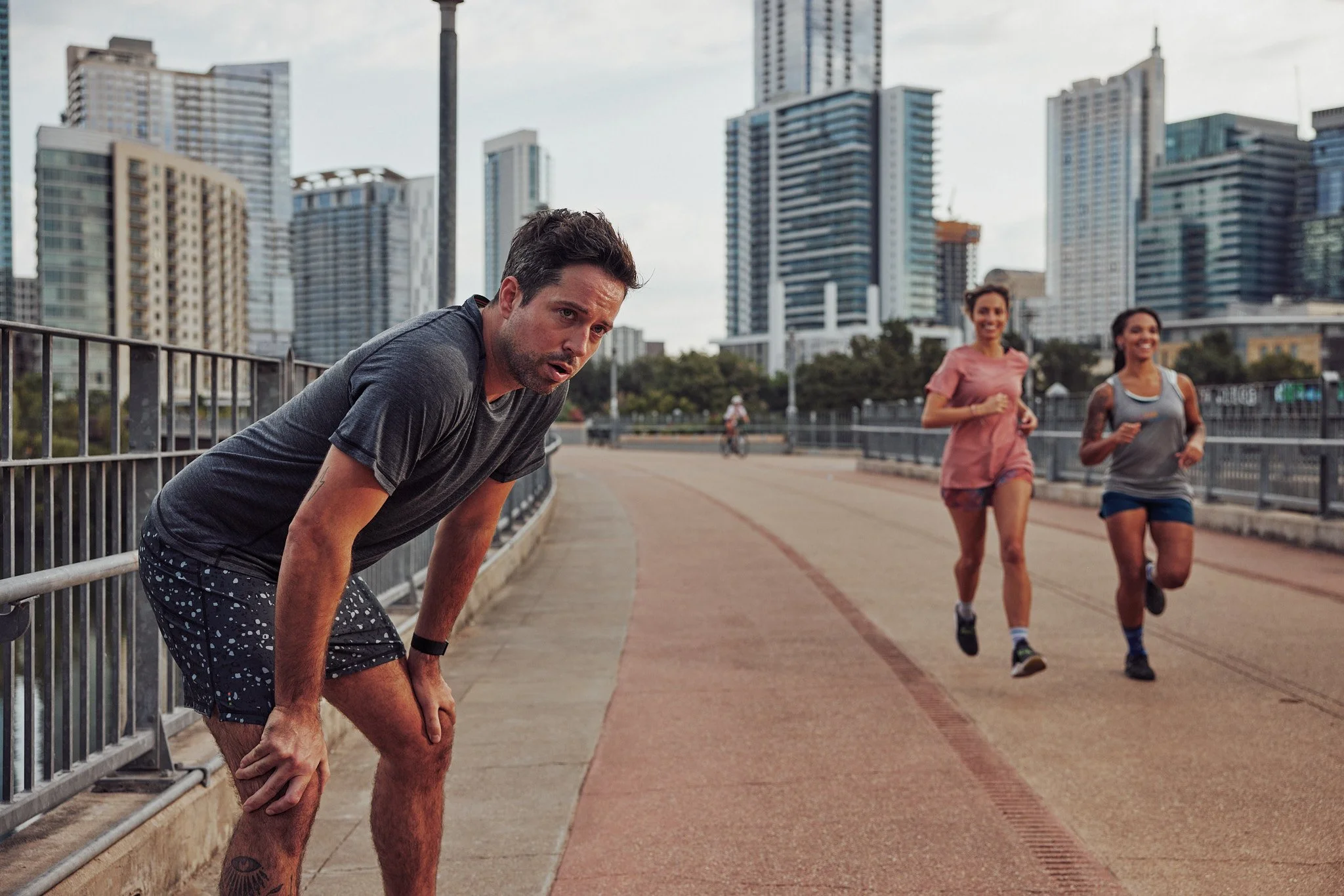 Runner stretching on a bridge with the Austin skyline behind, Smartwool Spring 2021 campaign, photography by Dag Larson