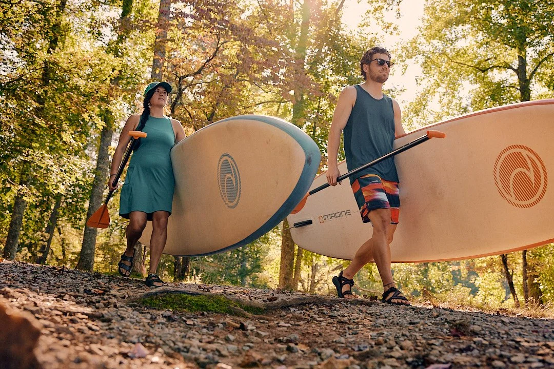 Friends carrying paddleboards through the woods to the lake near Asheville, North Carolina, Smartwool Spring 2023 campaign, photography by Dag Larson