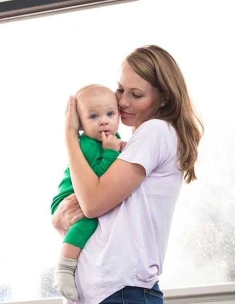A woman holding a baby with a finger in its mouth, both looking at the camera.