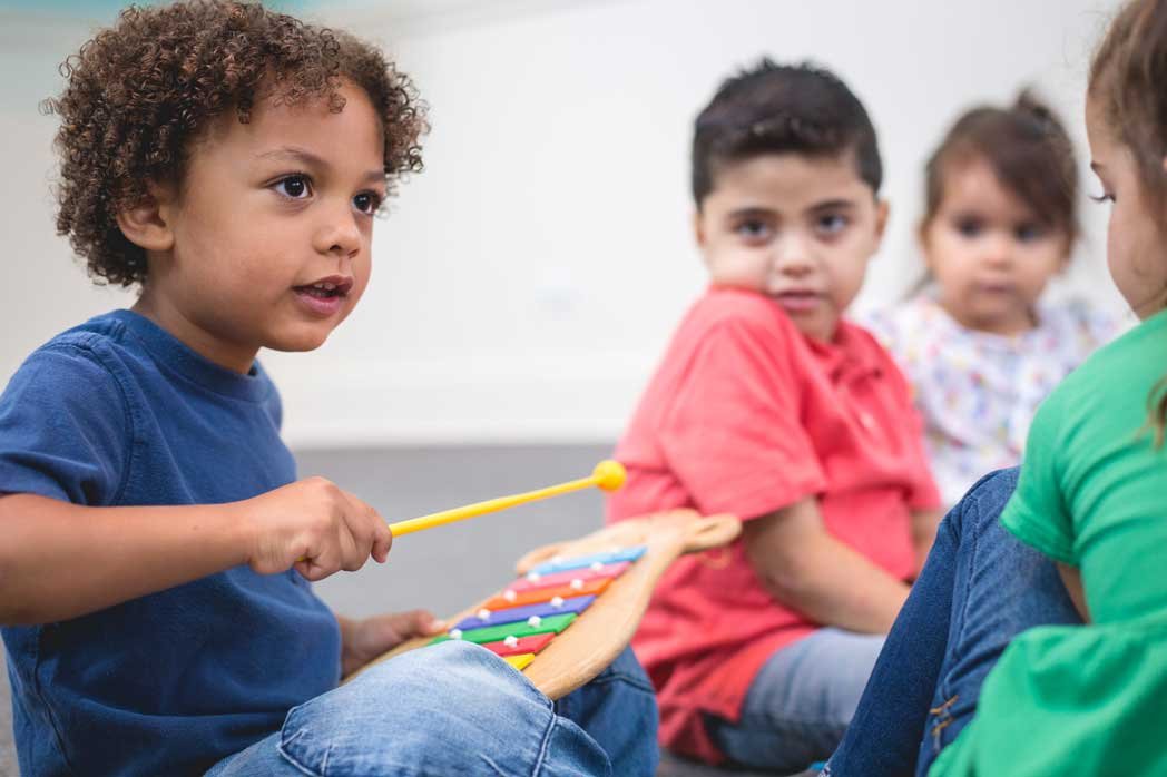 Children sitting in a circle, with one child playing a xylophone and others watching.
