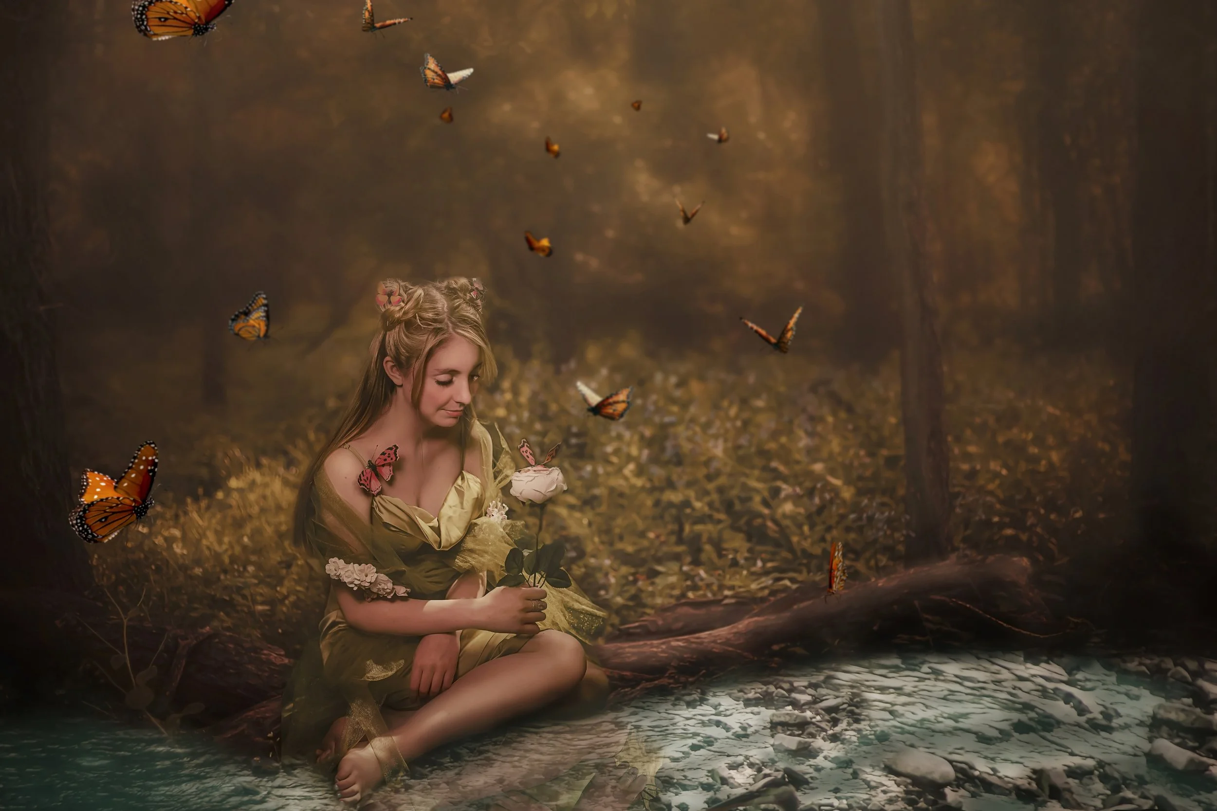 A young woman with long blonde hair, decorated with pink flowers, sits barefoot on a log by a small creek in a forest during autumn. She holds a white rose and appears to be gazing at it. Butterflies flutter around her, creating a magical, dreamy atmosphere.