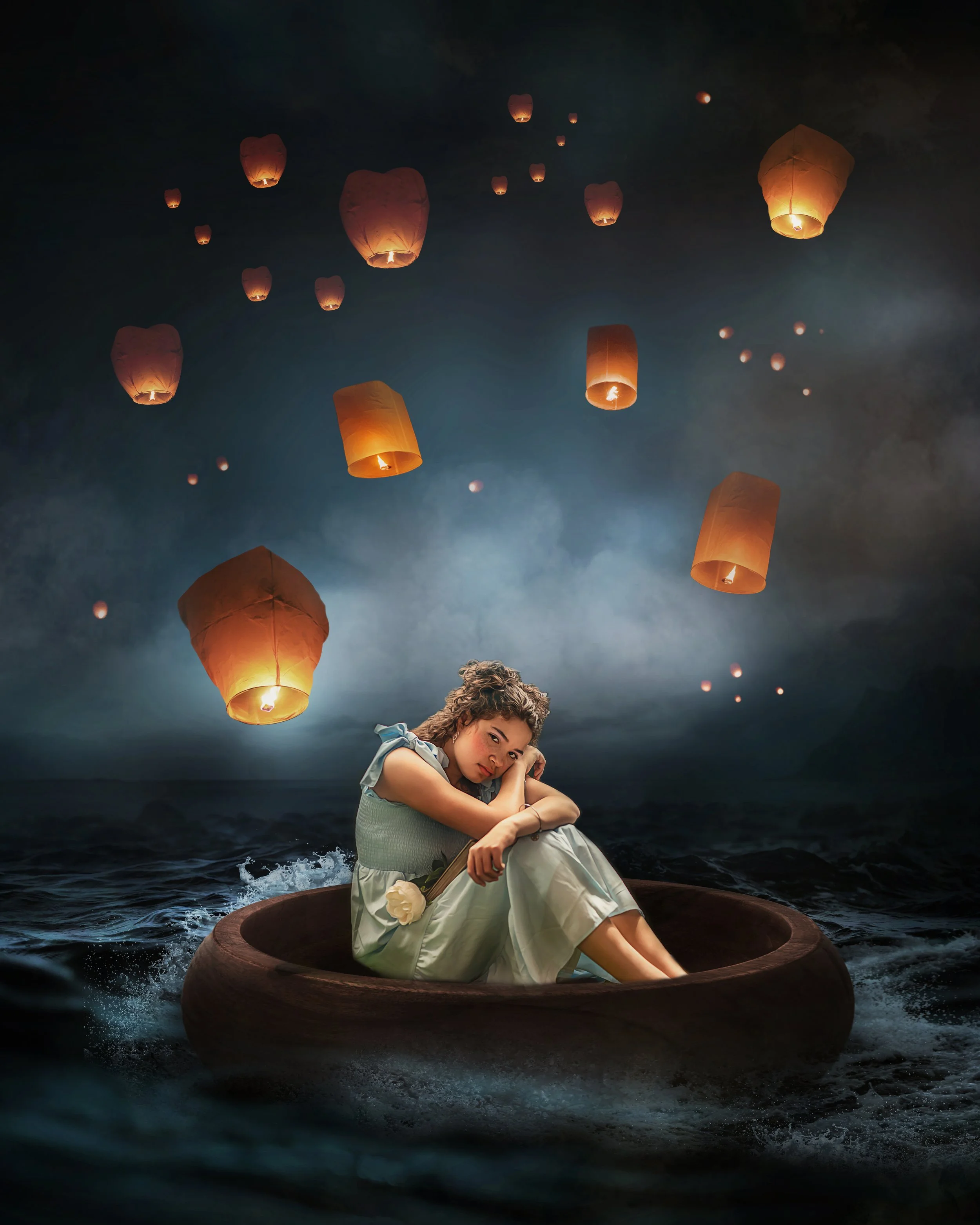 A young woman sitting in a small boat on dark water, holding a white rose, with sky filled with floating paper lanterns at night.