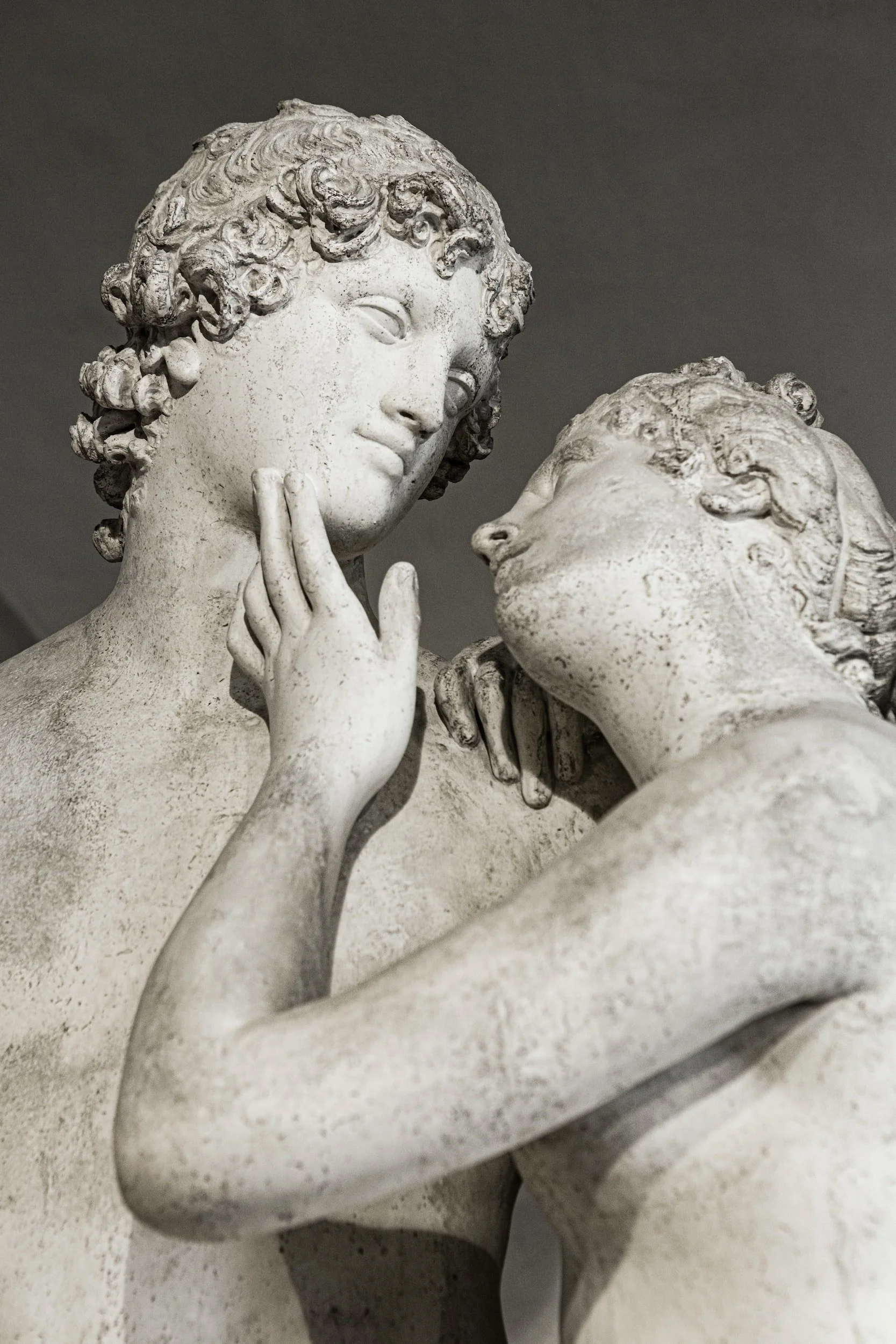 Close-up of a classical marble sculpture of two women with one touching the other's face and shoulder.