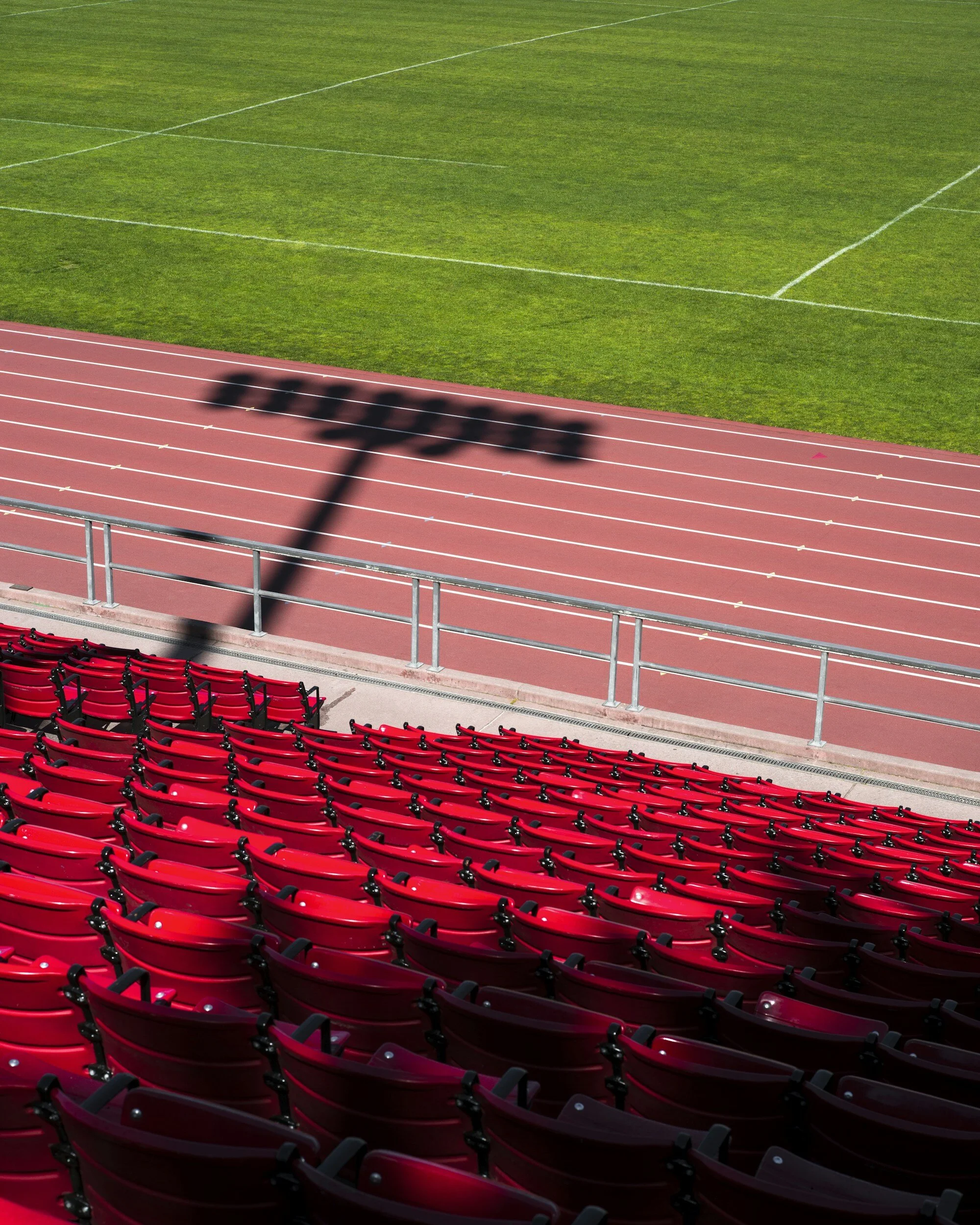 Empty red stadium seats and a running track with a shadow of a sign reading 'protest' cast over the track.