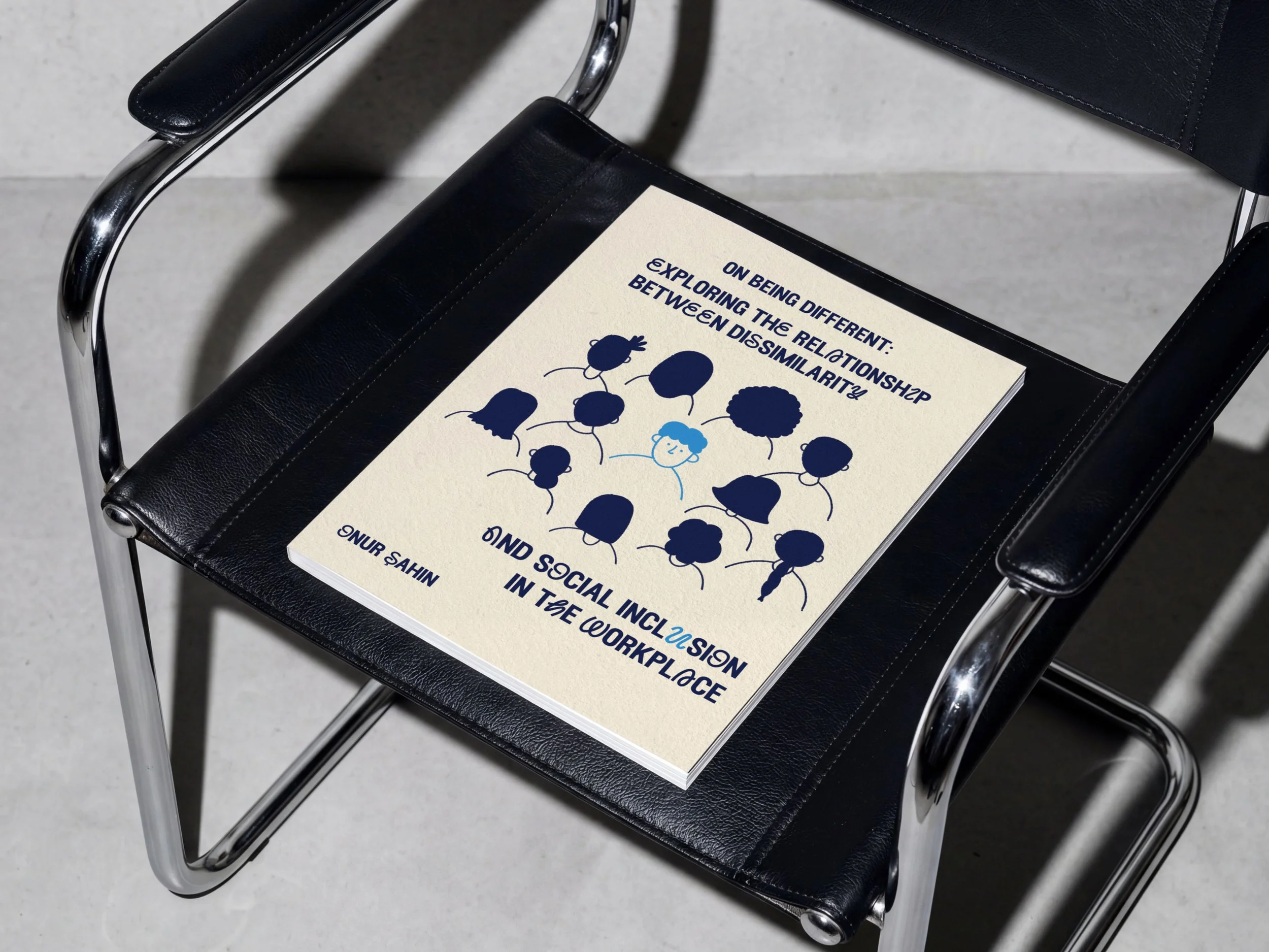 A black leather chair with chrome legs and armrests. On the seat of the chair is a white booklet with blue text and illustrations of people.