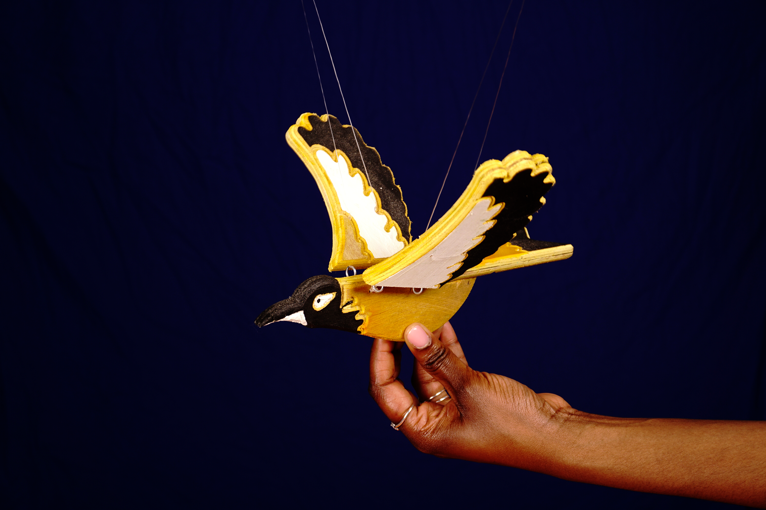 A person holding a wooden butterfly puppet with yellow, black, and white colors against a dark blue background.