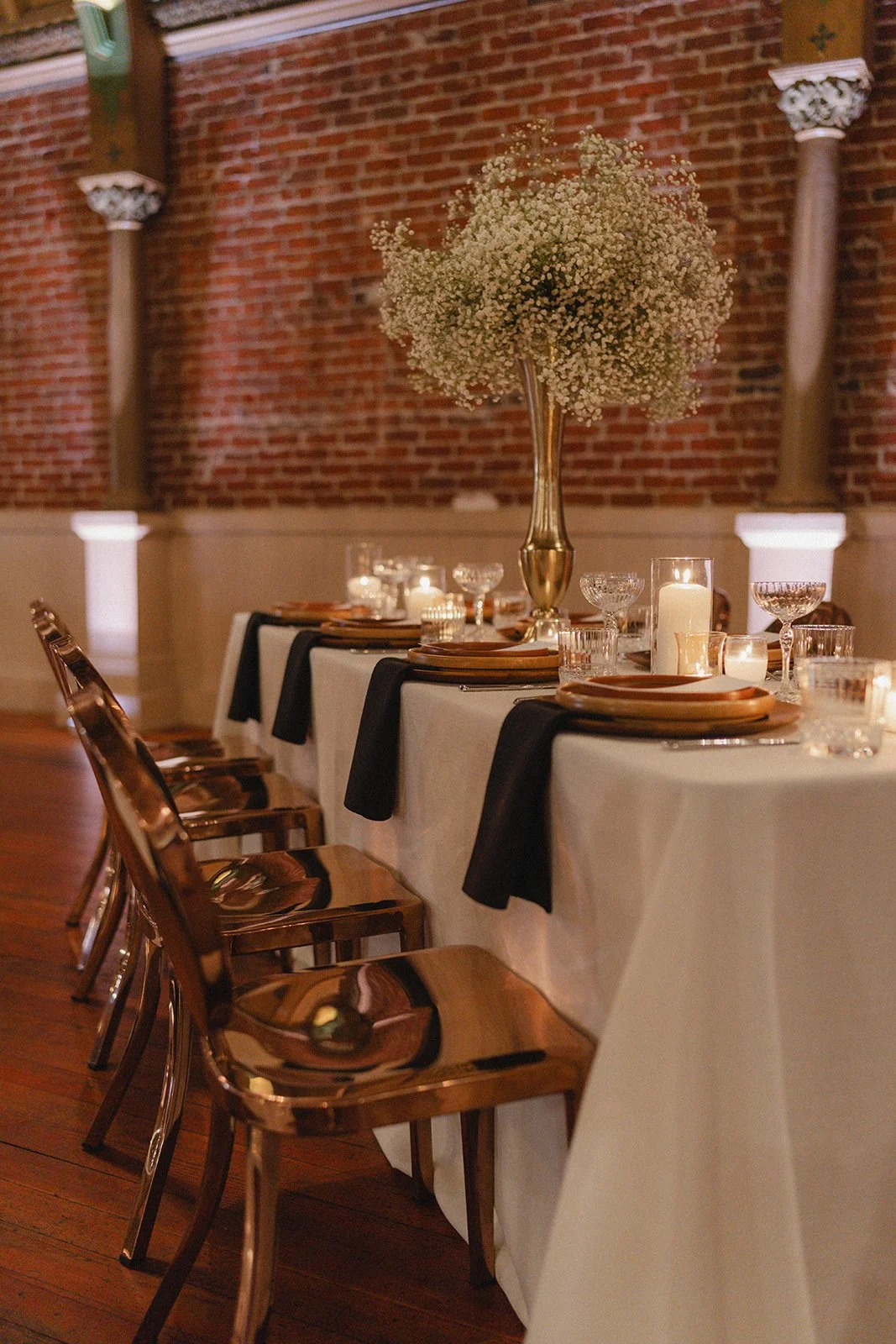 Detailed shot of a reception table, showcasing a flower arrangement and lit candles surrounded by formal place settings and crystal glassware.
