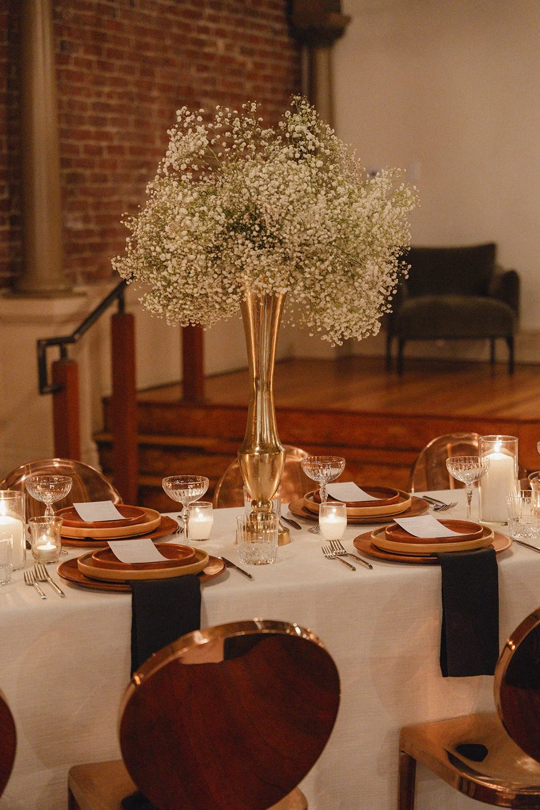 Detailed shot of a reception table centerpiece, showcasing a flower arrangement and lit candles surrounded by formal place settings and crystal glassware.