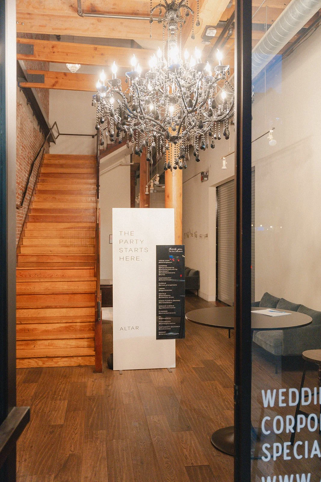 Grand entrance lobby and staircase at Altar Long Beach, featuring a prominent chandelier and a welcoming sign that reads, "The party starts here."