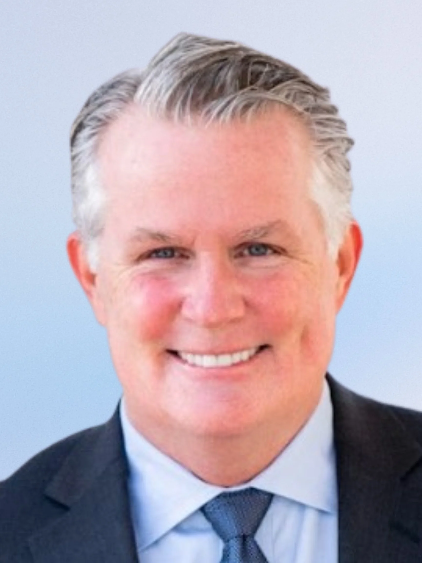 Black and white headshot of a man in a suit and tie smiling.