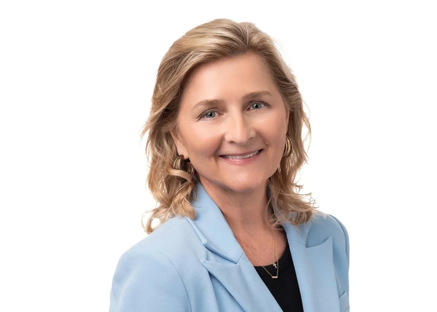 A black and white portrait of a woman with shoulder-length wavy hair, wearing a light-colored blazer over a dark top, smiling at the camera.