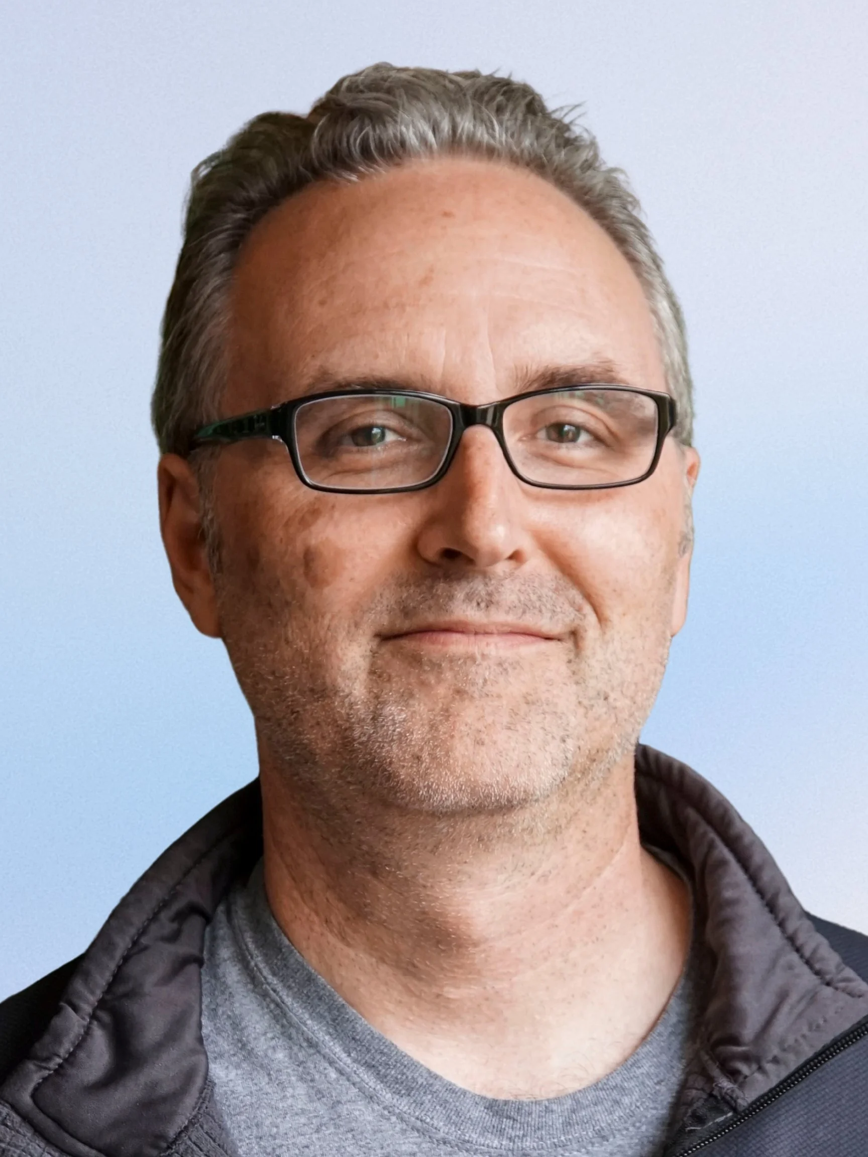 Black and white photo of a man wearing glasses, smiling, with a background of palm leaves.