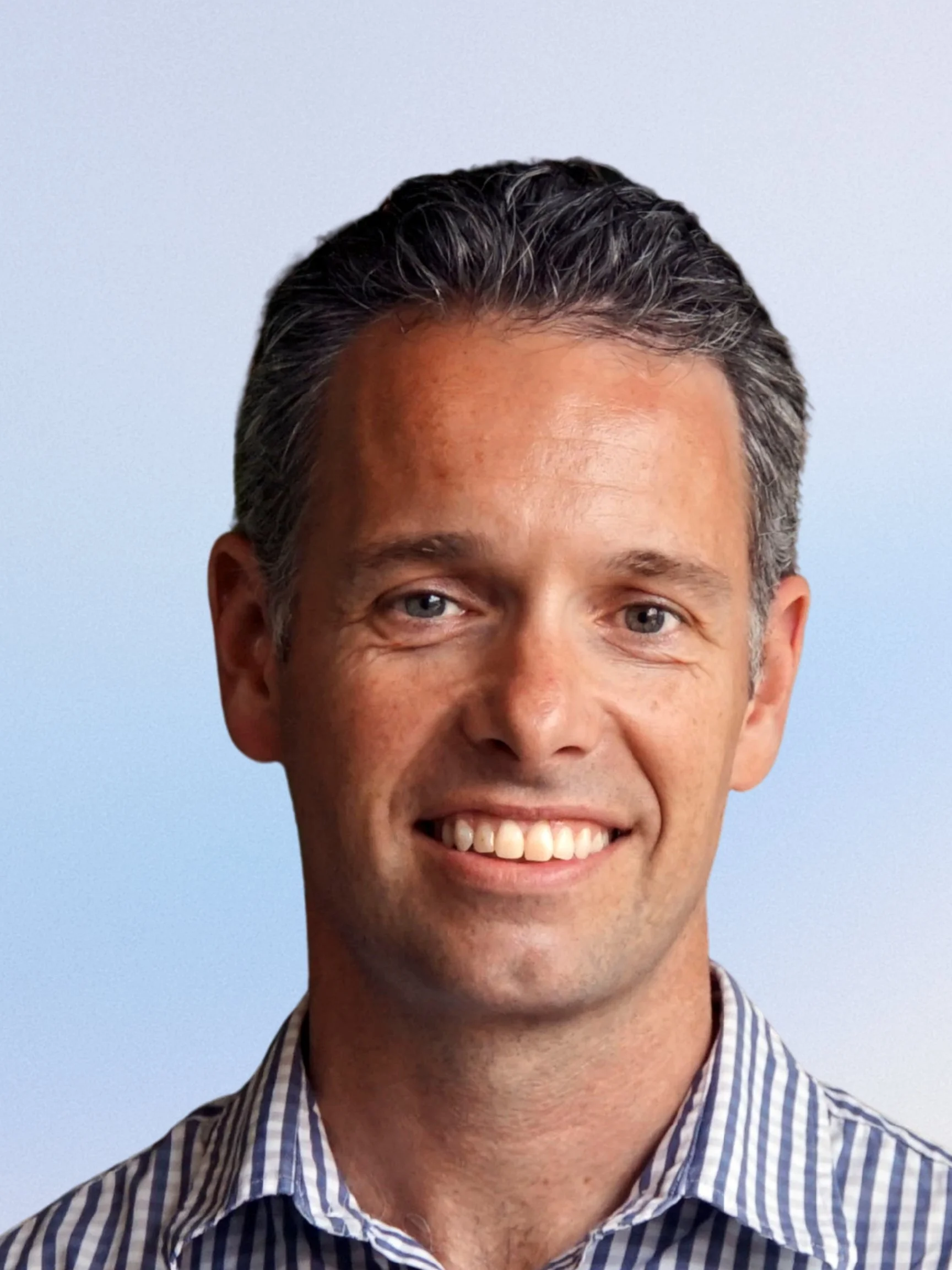 Young man with short hair smiling, background has potted plants.