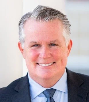 Black and white headshot of a man in a suit and tie smiling.