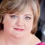 Close-up of a woman's face with short blonde hair and blue eyes.