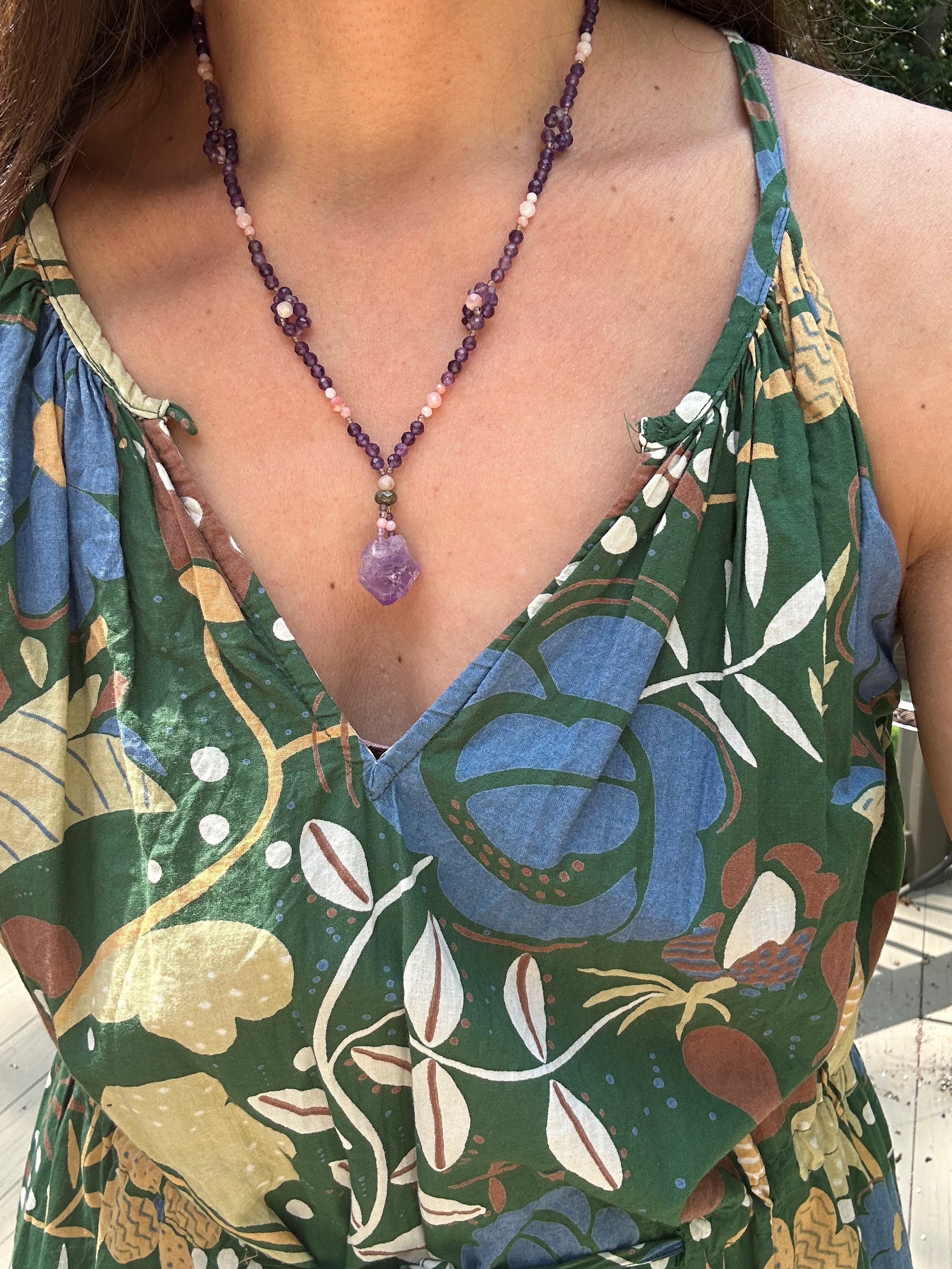 A raw faceted amethyst stone hangs on an 18 inch necklace of Amethyst and Pink Opal flowers. Worn with an earth-tone dress