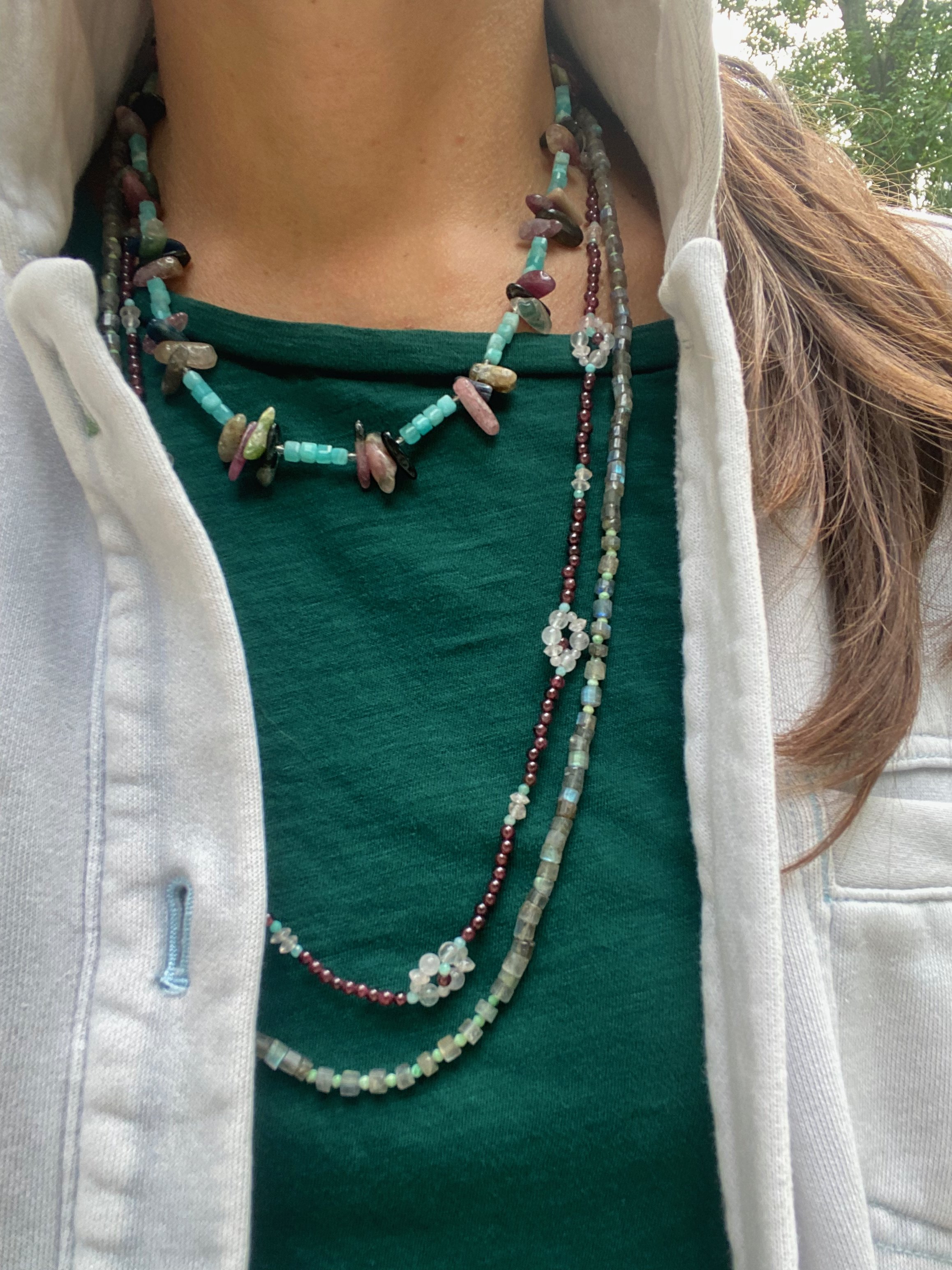Apatachi handcrafted bohemian necklace. Rose Quartz Wildflowers on a long necklace of Garnet gemstones with Amazonite and pyrite. Layered with other necklaces on a green shirt