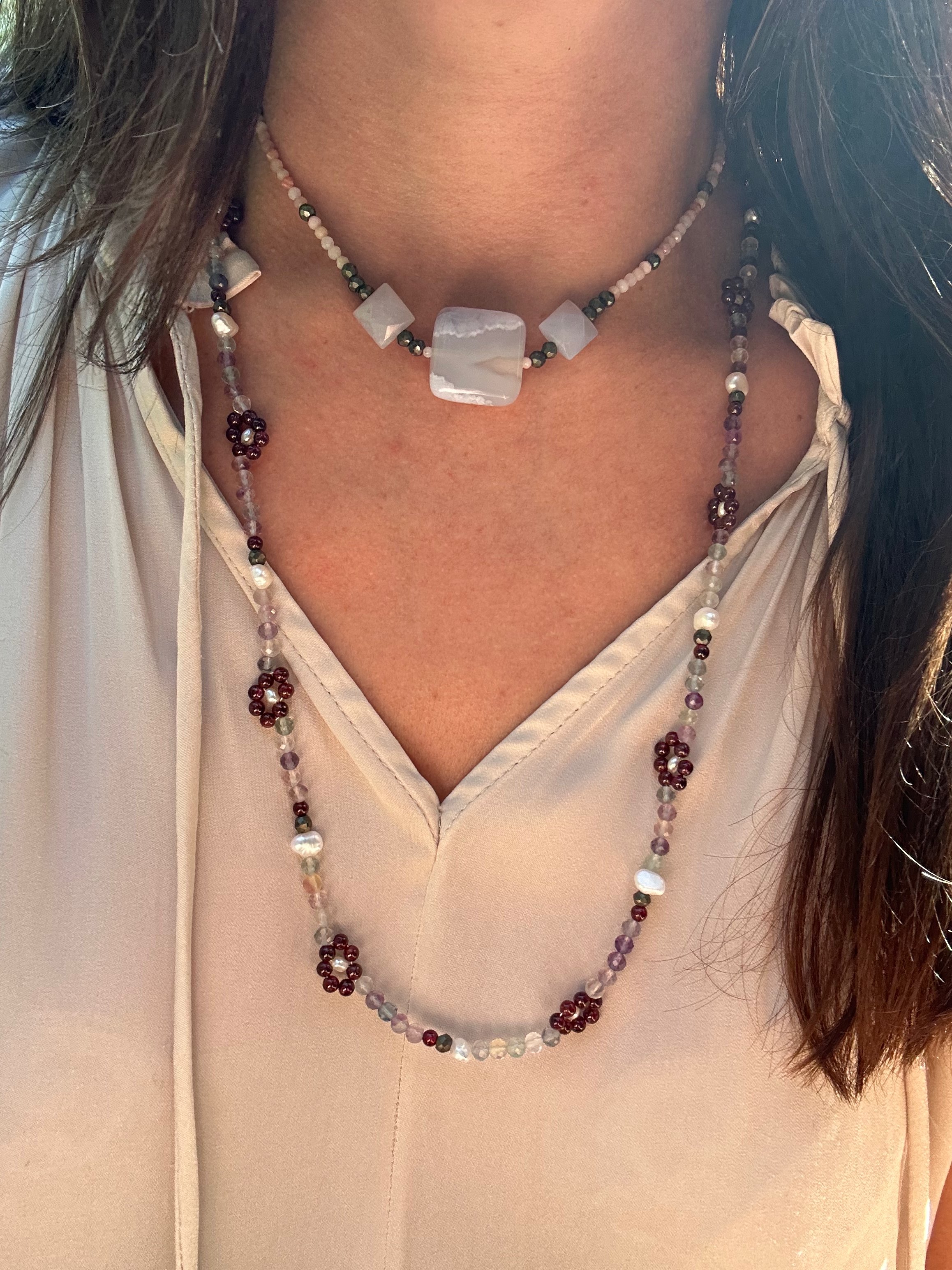 Petite garnet wildflowers make a statement alongside freshwater pearl accents and shimmering rainbow flourite in this beautiful long necklace. Paired with a shorter necklace on a dressy white top.