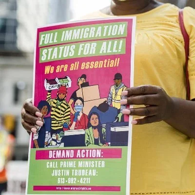 Photo of someone holding a poster that reads Full Immigration Status for All