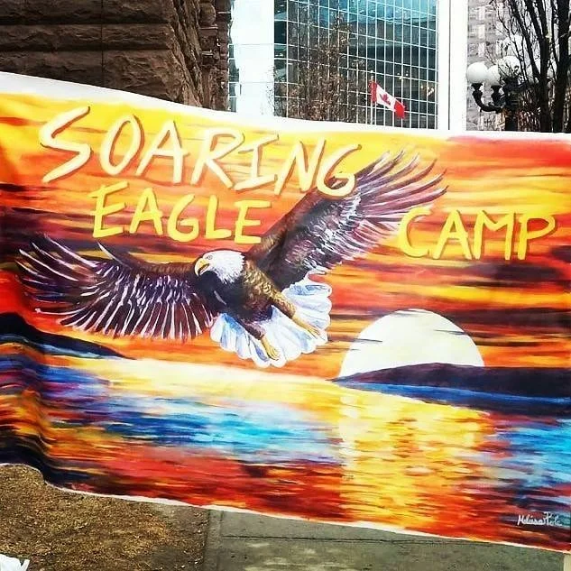 A photo of a painted banner with a flying eagle and a sunset with the text Soaring Eagle's Camp