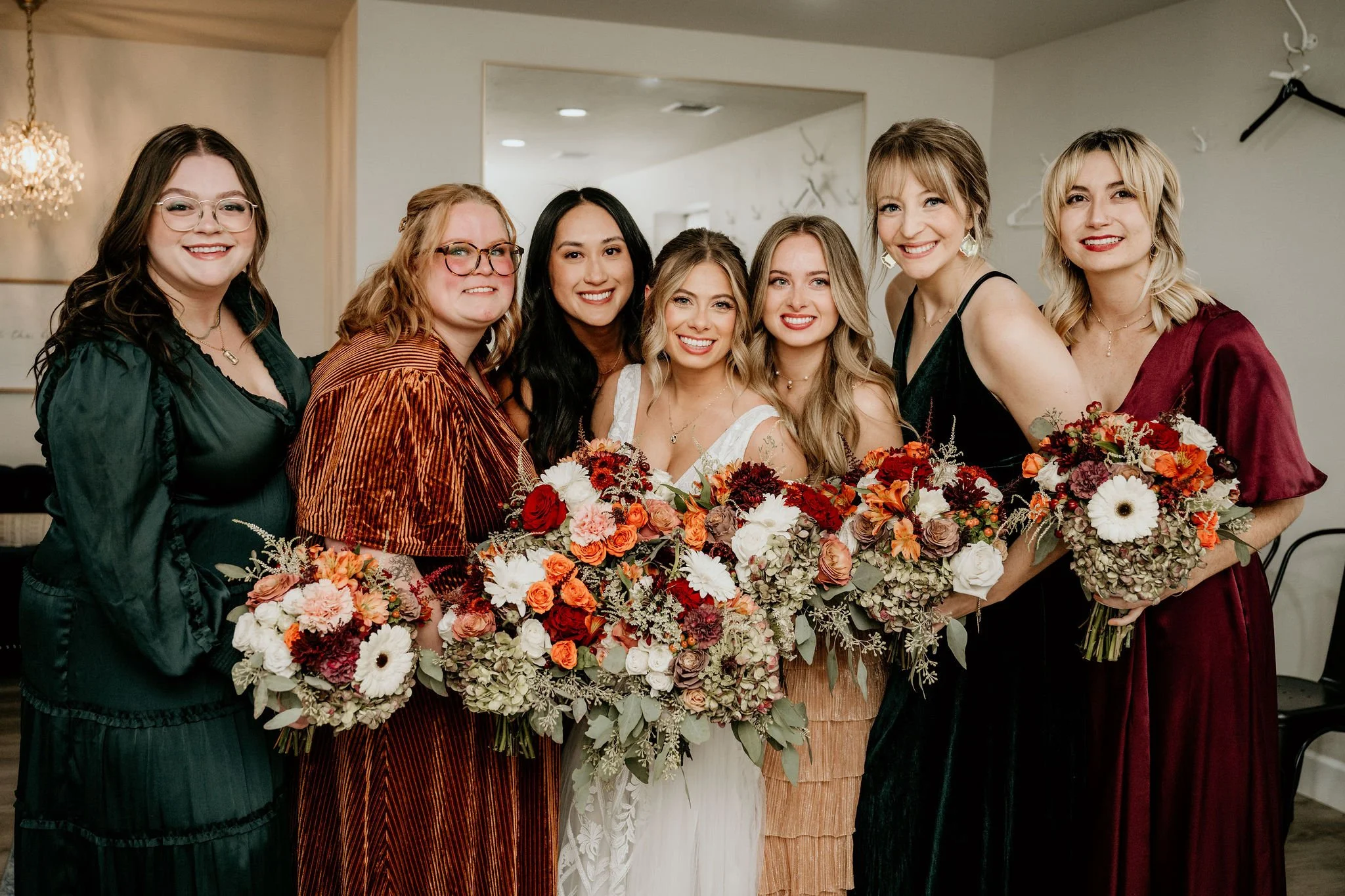 Group of seven women holding bouquets of flowers at a celebration or wedding indoors.