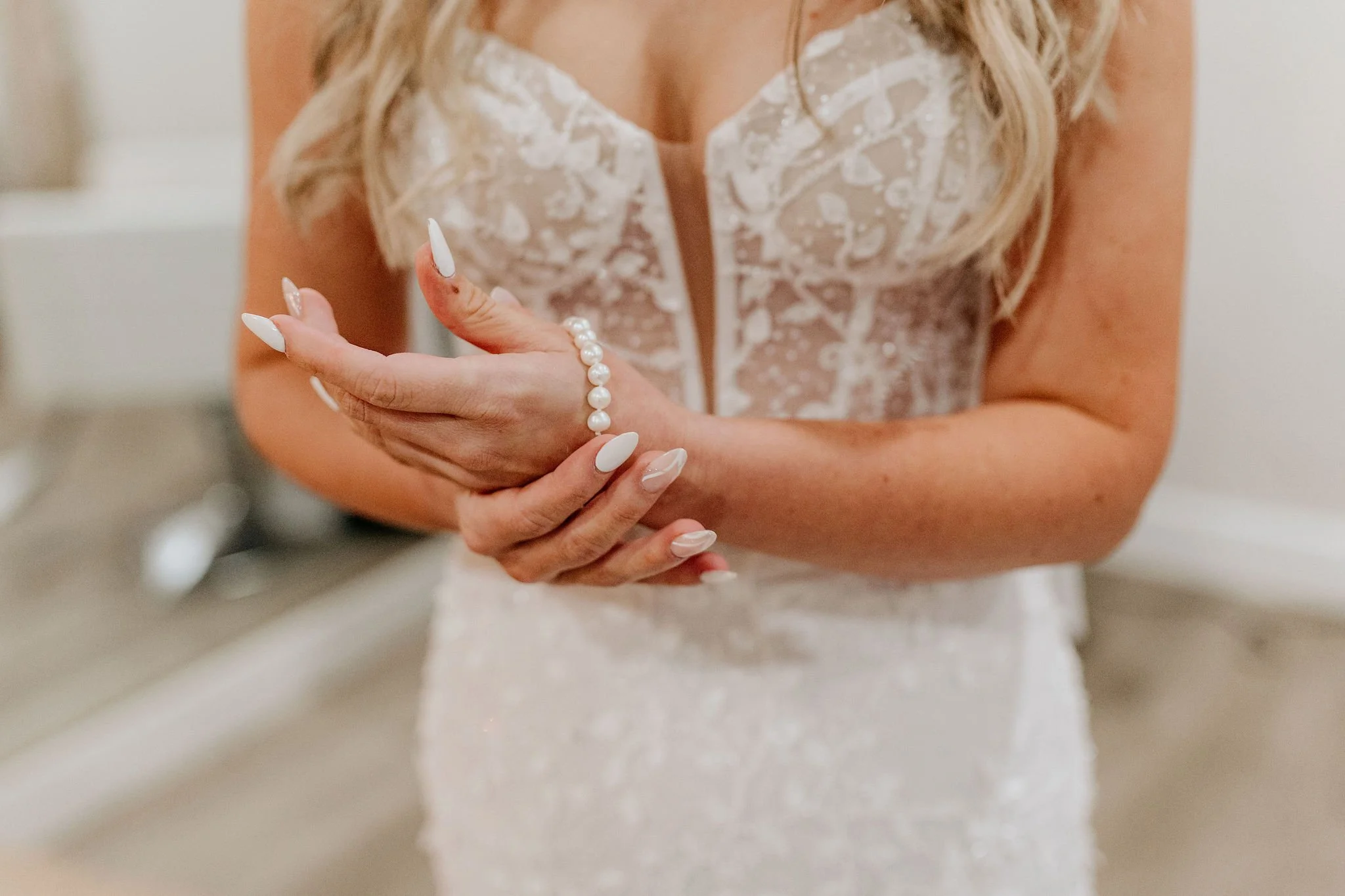 Close-up of a woman in a wedding dress, holding a pearl bracelet on her wrist.