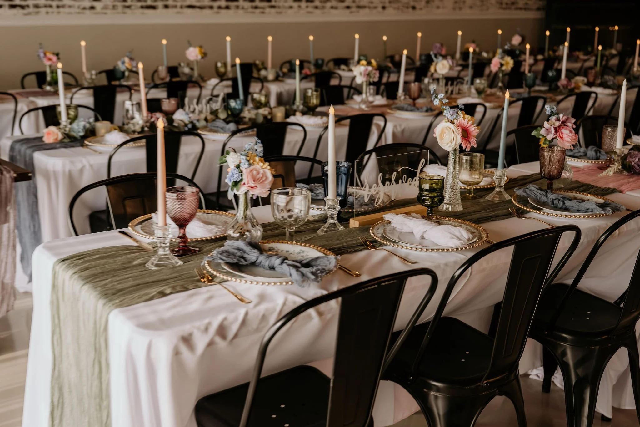 Long banquet tables decorated with candles, floral arrangements, and elegant tableware, set for a formal event or wedding reception.