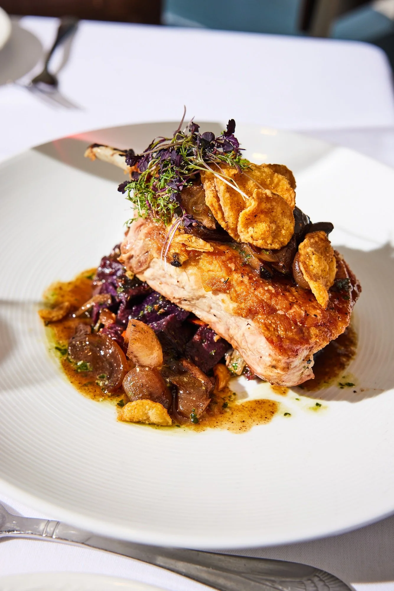 A plated dish featuring a piece of cooked chicken breast topped with fried garnish and herbs, served over a bed of cooked vegetables and sauce.
