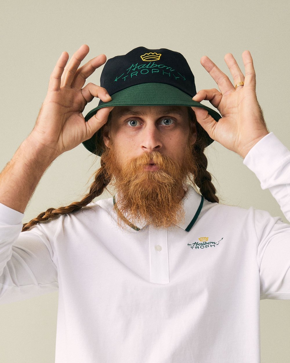 A man with red hair and a beard wearing a white polo shirt and adjusting a baseball cap that says "Mabon Trophy" on it.