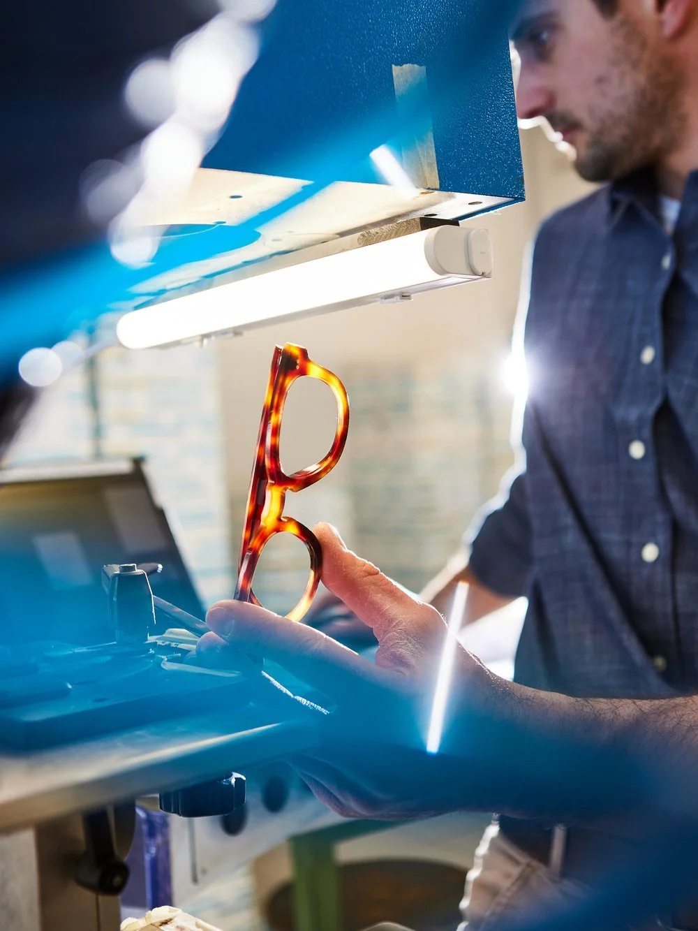 A person holding a pair of tortoise shell sunglasses while working at a machine in a workshop.