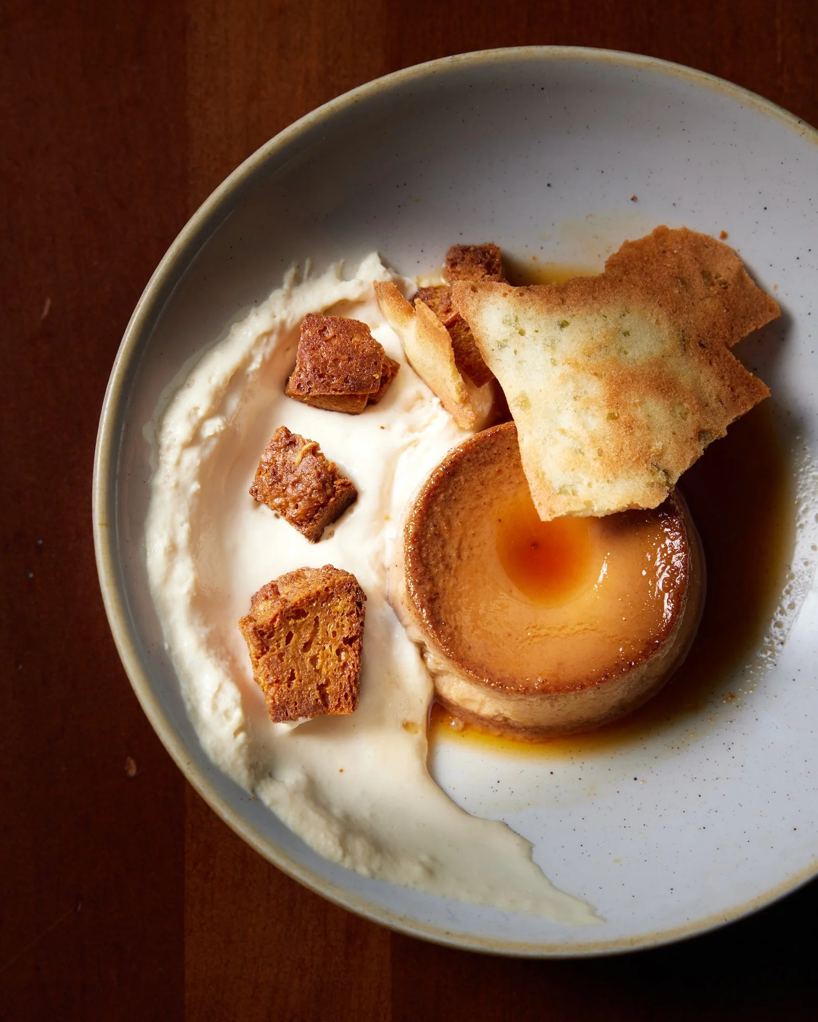 A bowl with flan, whipped cream, croutons, and a piece of toasted bread.
