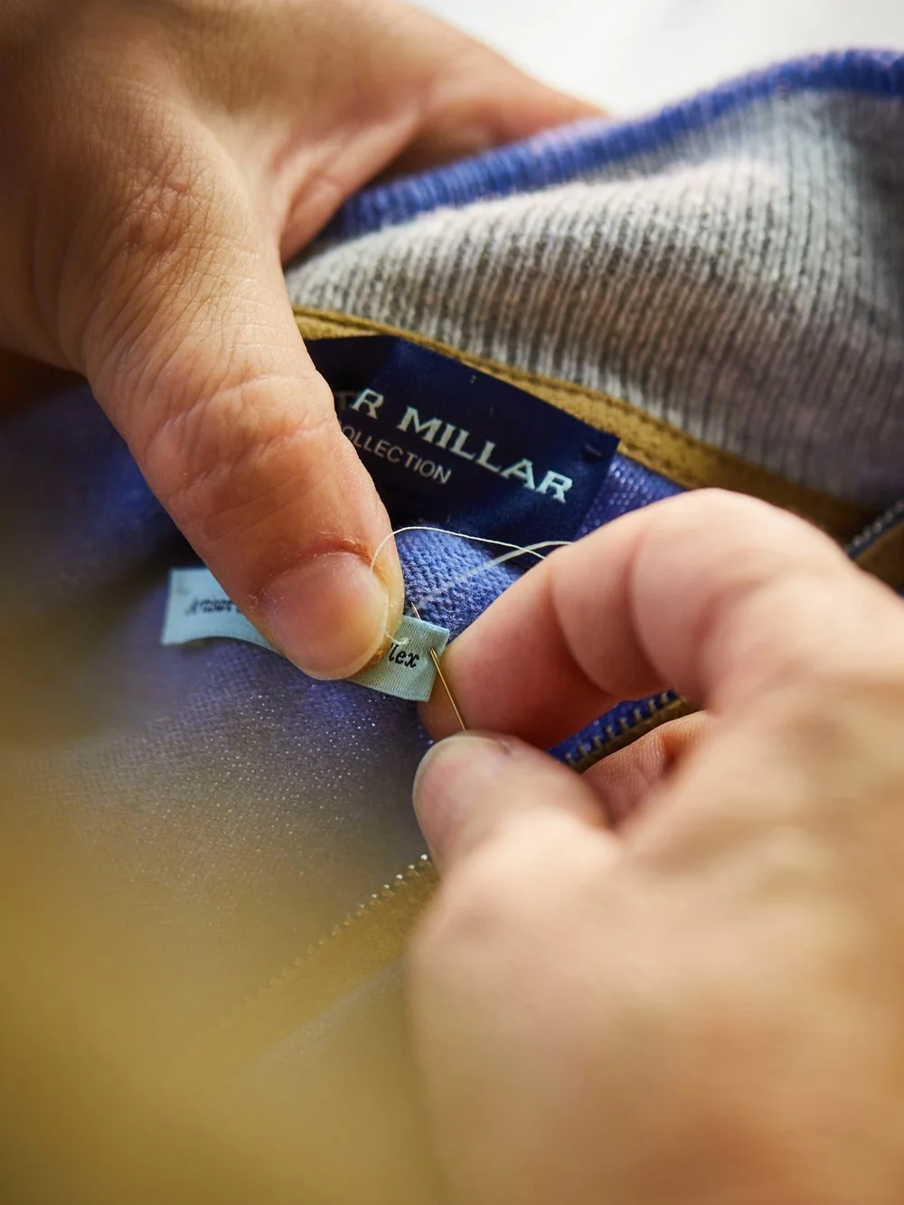 Close-up of a person sewing a label onto a clothing item, with visible interior tags reading 'Walter Miliar.'