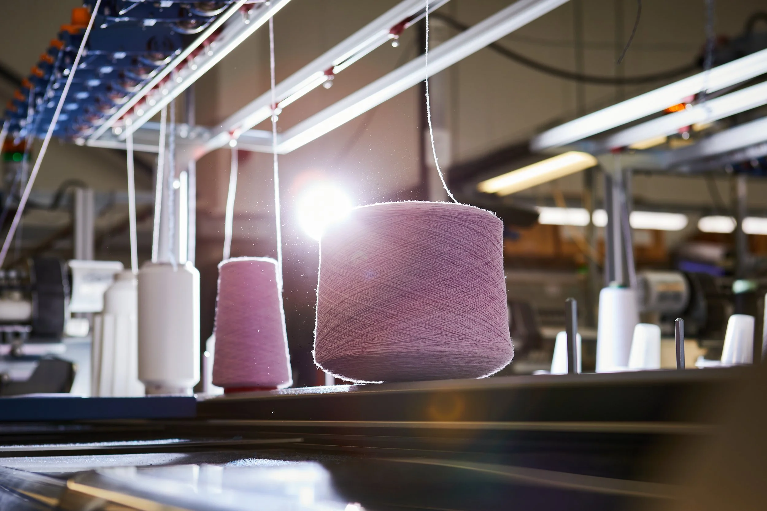 Spools of pink and white thread on a sewing machine in a textile factory with bright lighting.