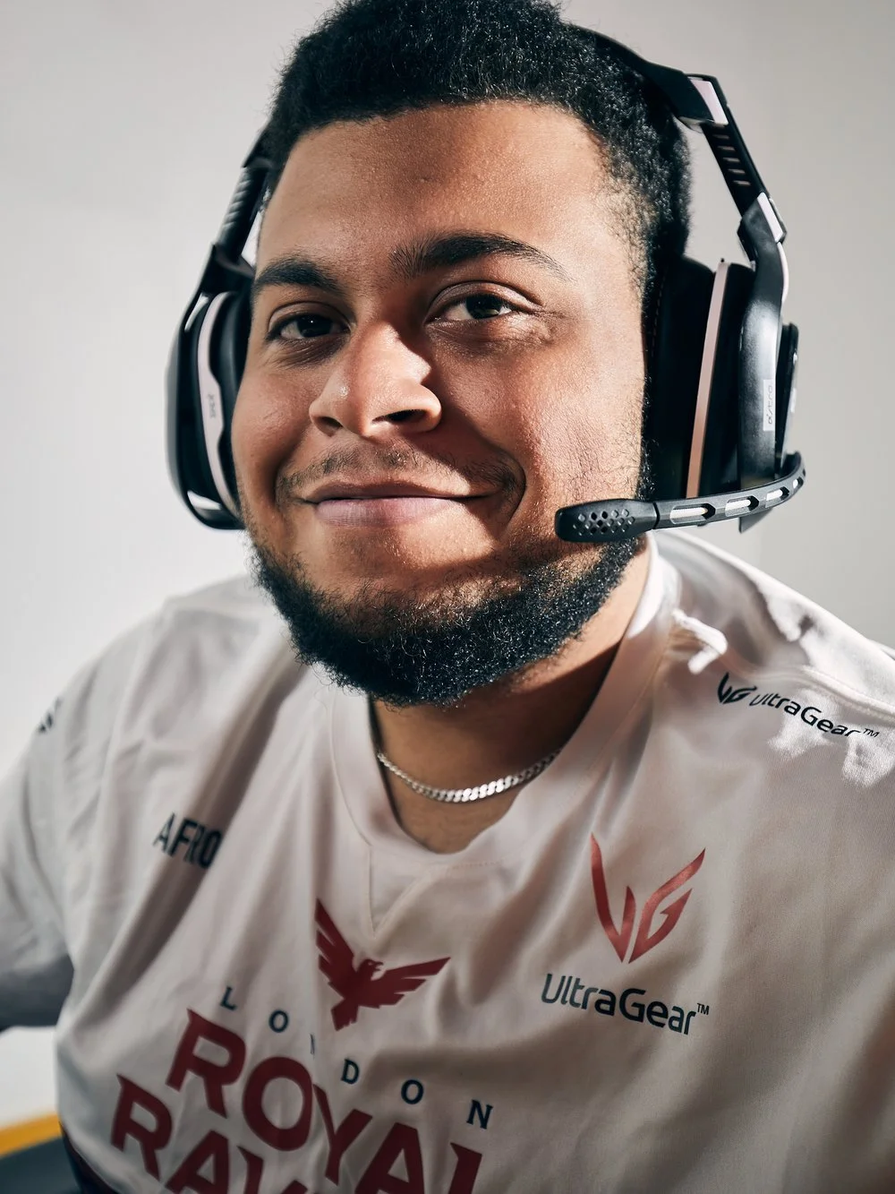 Close-up of a smiling man wearing a gaming headset and a white esports jersey with logos.
