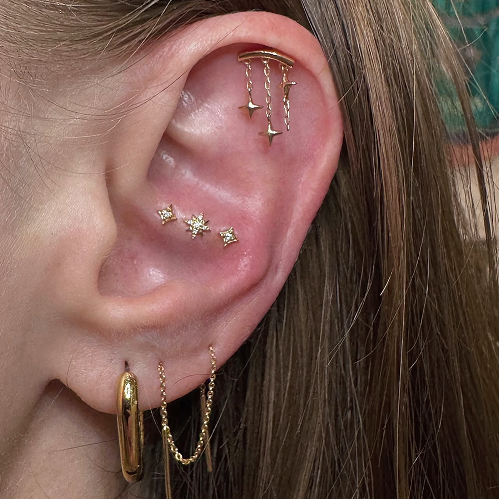 an ear with gold and diamond jewelry, specifially three star studs across the conch.